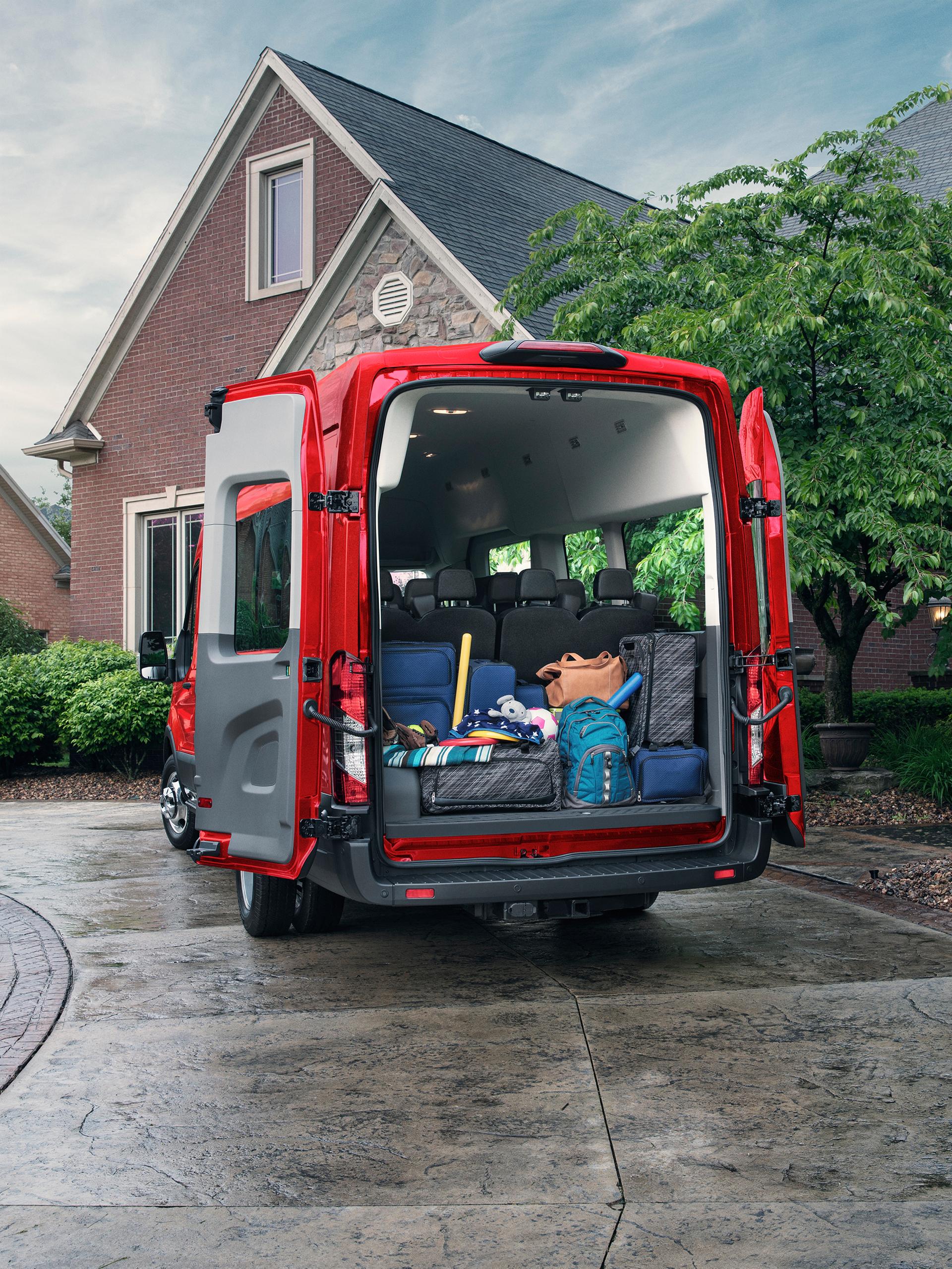 Fourgonnette Ford Transit® 2027 rouge, avec les portes arrière ouvertes et la zone de chargement remplie de divers articles, stationné devant une maison