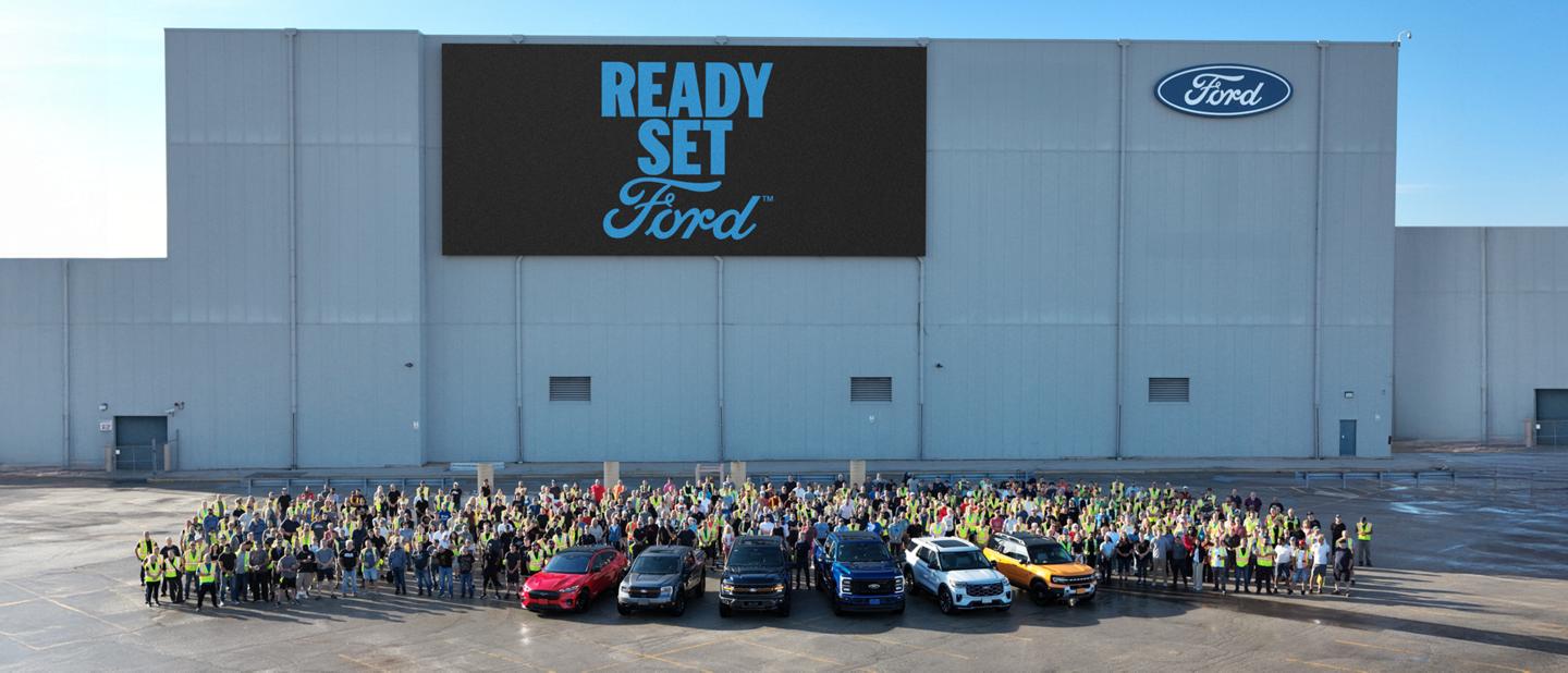 Plan large de six véhicules Ford devant un grand groupe d’employés Ford à l’usine