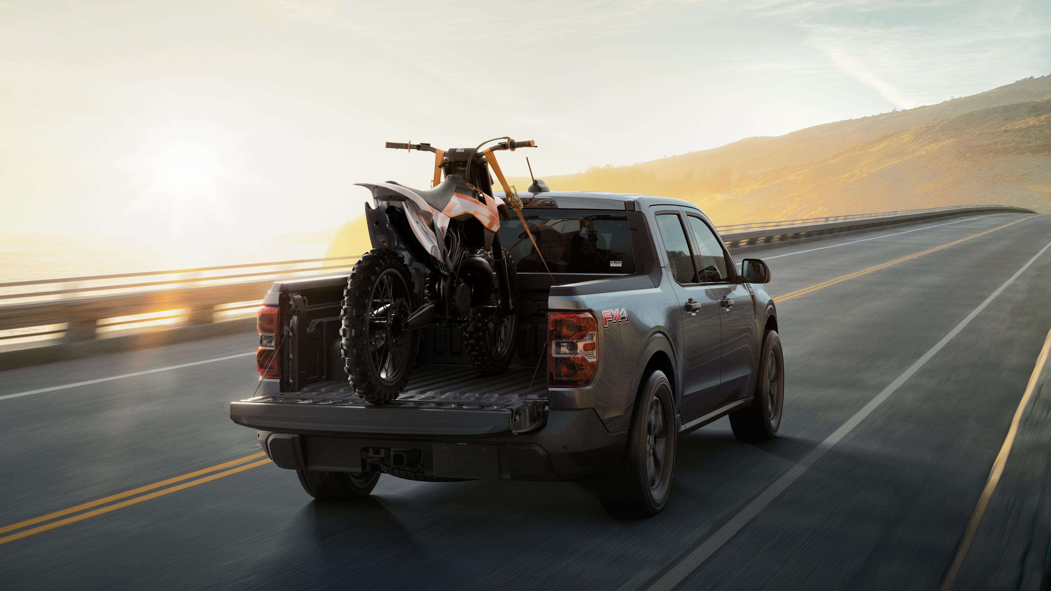 Camionnette Ford Maverick® 2026 avec une moto tout-terrain arrimée dans la caisse, roulant sur une autoroute au lever du soleil.