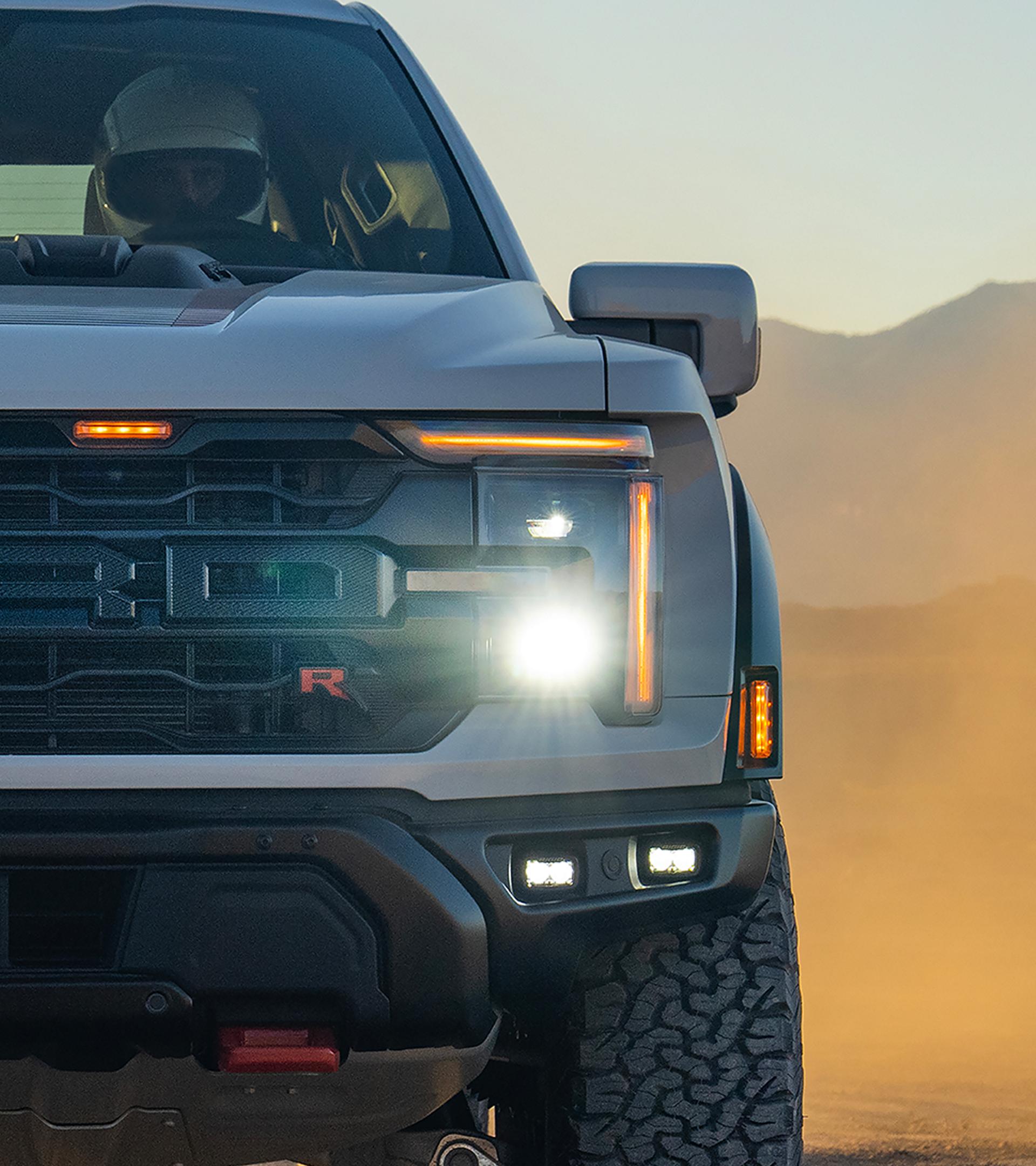 Gros plan sur la calandre et les phares d’un camion Ford F-150® Raptor® 2026 conduit dans le désert