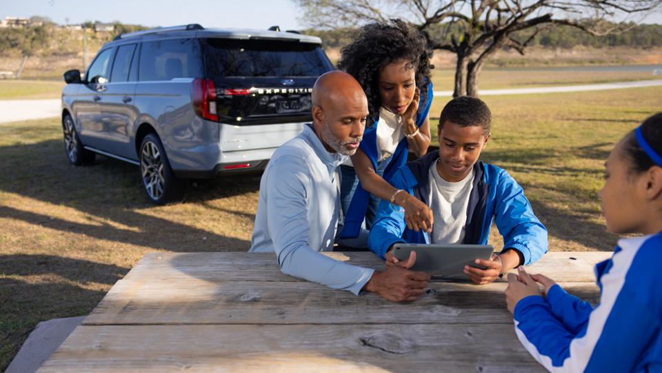 Trois personnes utilisant le point d'accès sans fil Wi-Fi® avec un VUS Ford Expedition® 2027 stationné en arrière-plan