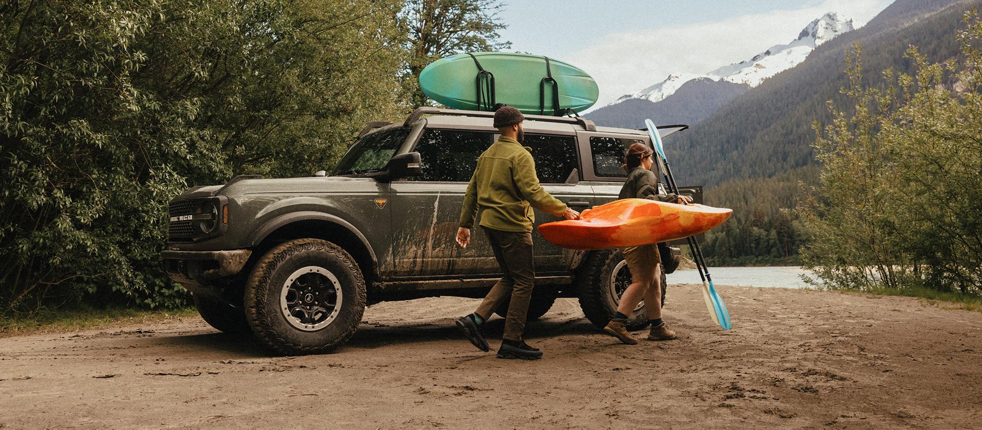 Un homme et une femme transportant un kayak et une pagaie s’éloignent d’un VUS Ford Bronco® 2026 garé sur une vasière