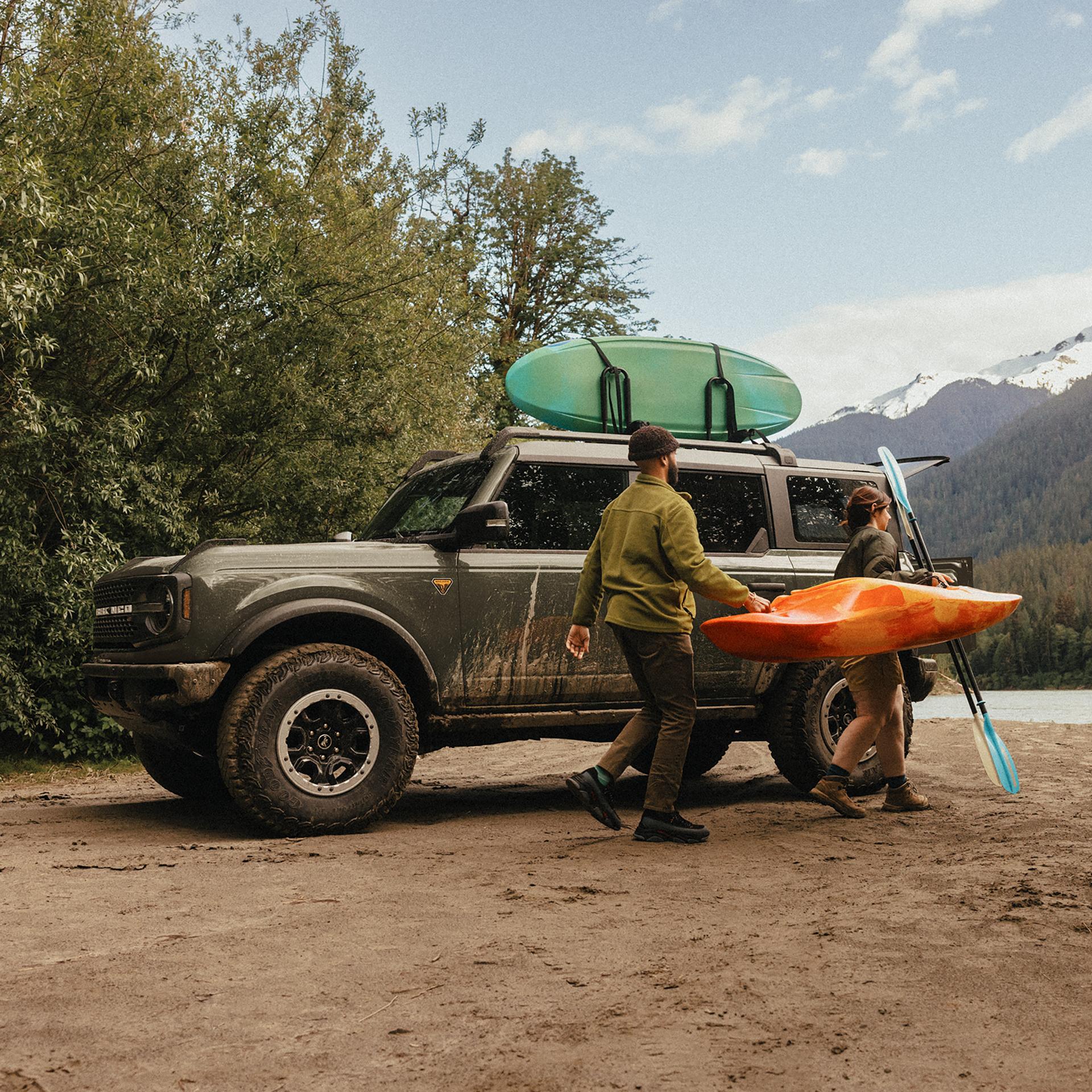 Un homme et une femme transportant un kayak et une pagaie s’éloignent d’un VUS Ford Bronco® 2026 garé sur une vasière