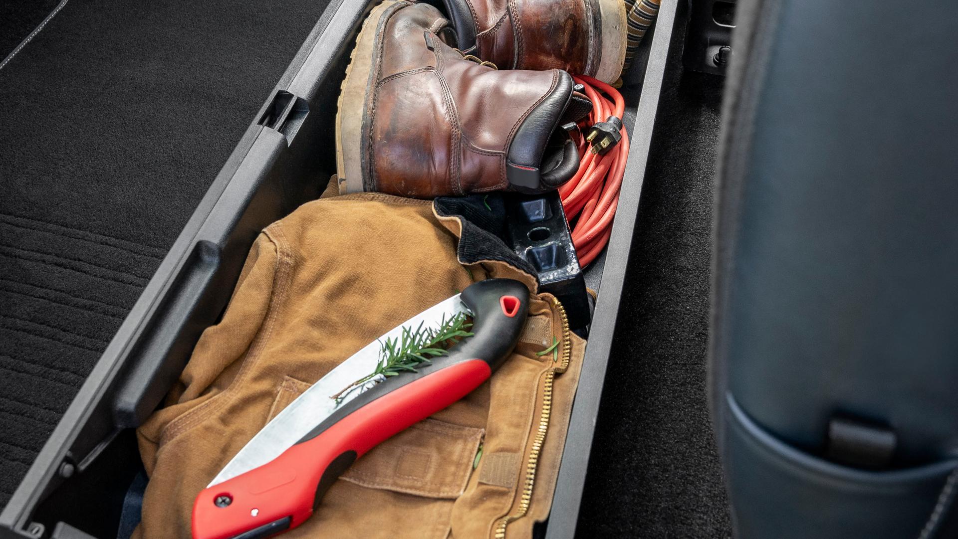 Boîte de rangement sous le siège arrière ouverte et remplie d’outils et d’équipement