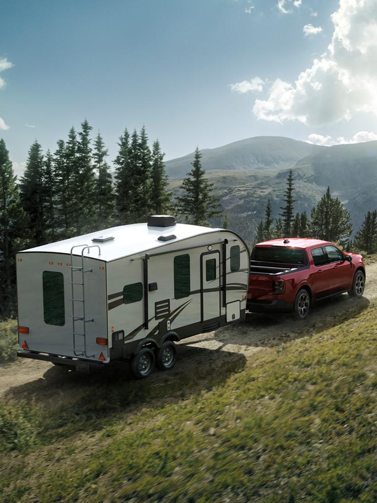 Une camionnette Ford Maverick® 2026 tirant une caravane sur une colline sur une route de gravier