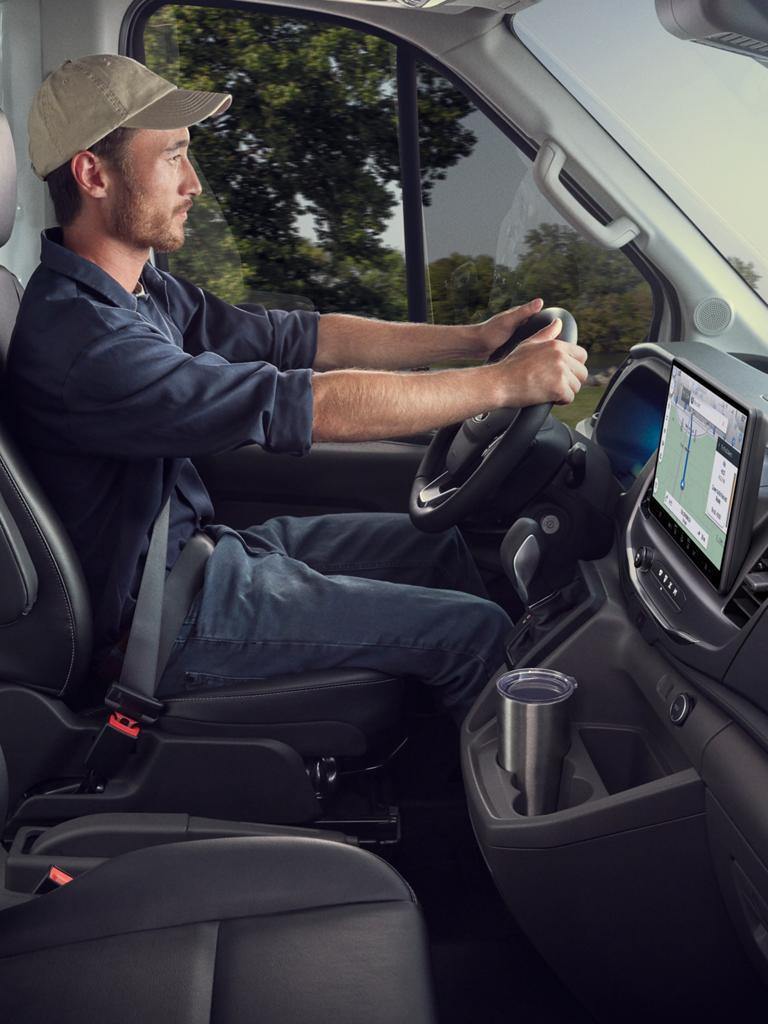 Une fourgonnette utilitaire Ford Transit® 2027 rouge roulant sur une route mouillée sous la pluie, sous un ciel sombre et orageux