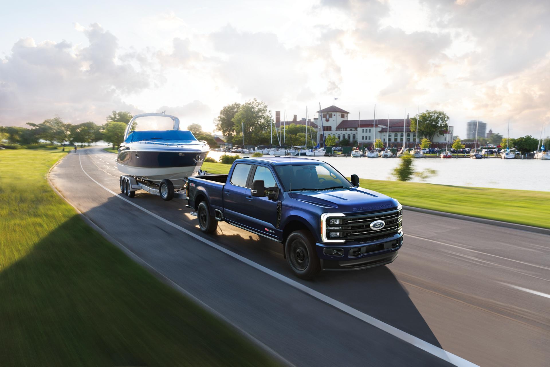 Modèle Ford Super Duty® F-350® Platinum® 2026 en bleu argon remorquant un bateau à moteur sur une route pavée