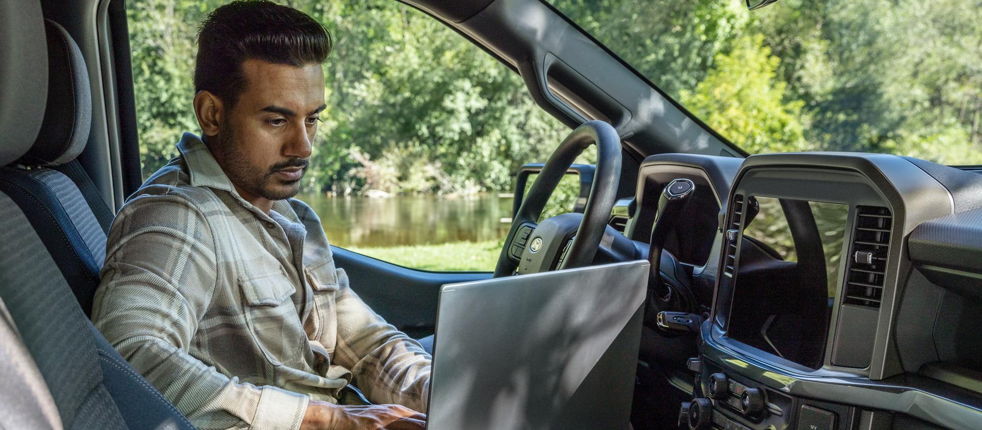 Une personne assise dans une cabine du Ford F-150® 2025 travaillant sur un ordinateur portable utilisant la surface de travail intérieure 