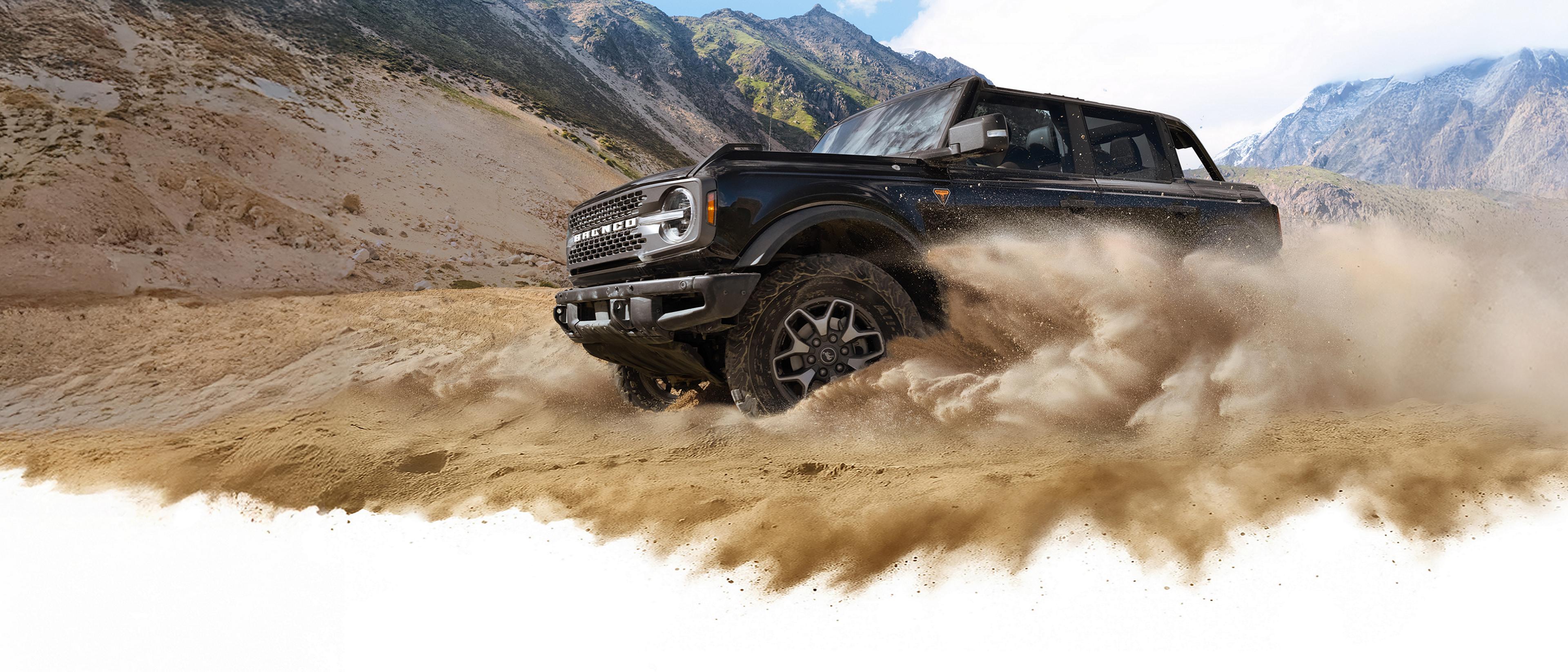 Un VUS Ford Bronco® 2026 soulève la poussière dans une vallée au pied de collines rocheuses