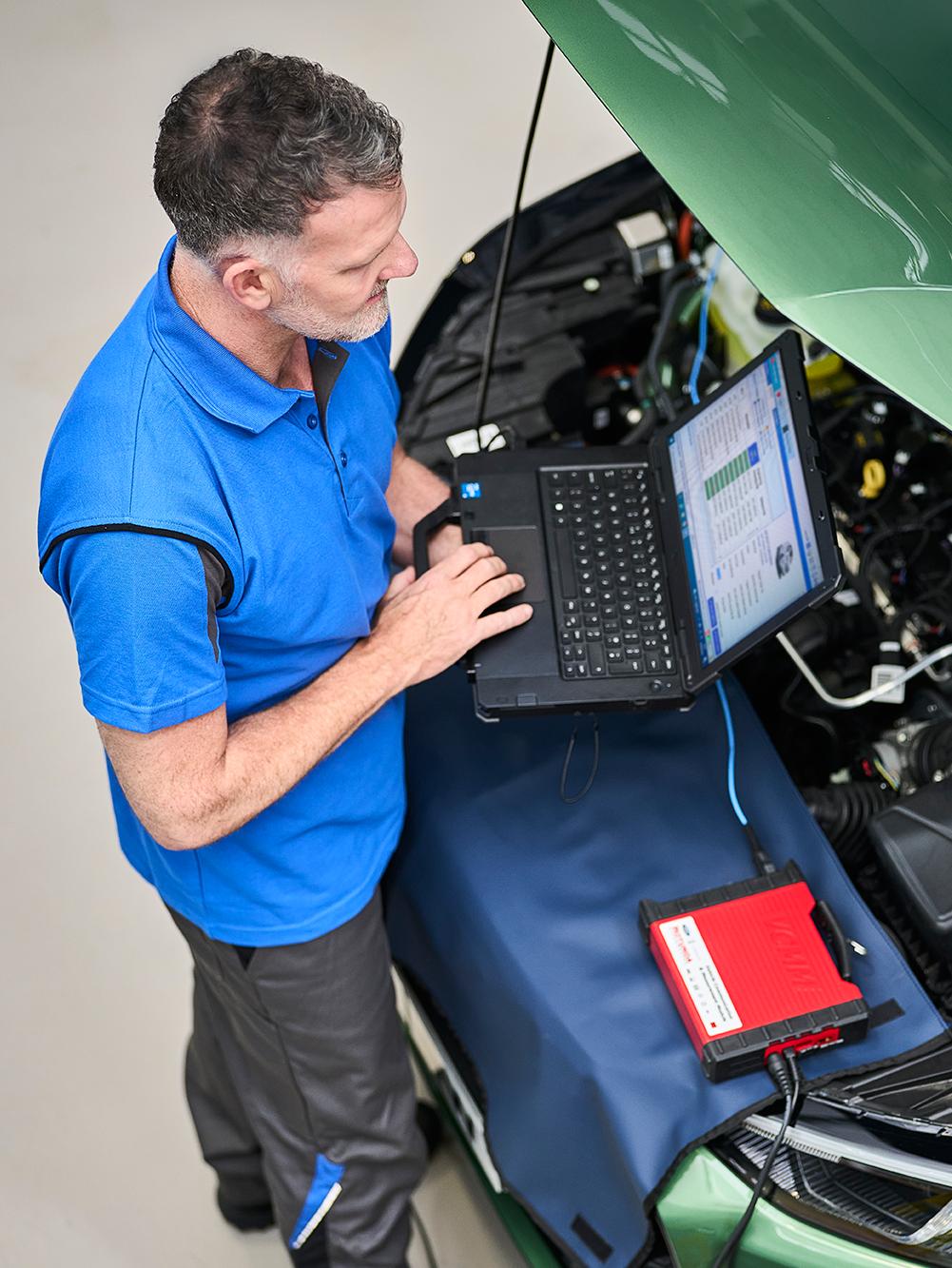 Un technicien d'entretien inspecte un véhicule Ford à l'aide d'un ordinateur portable.