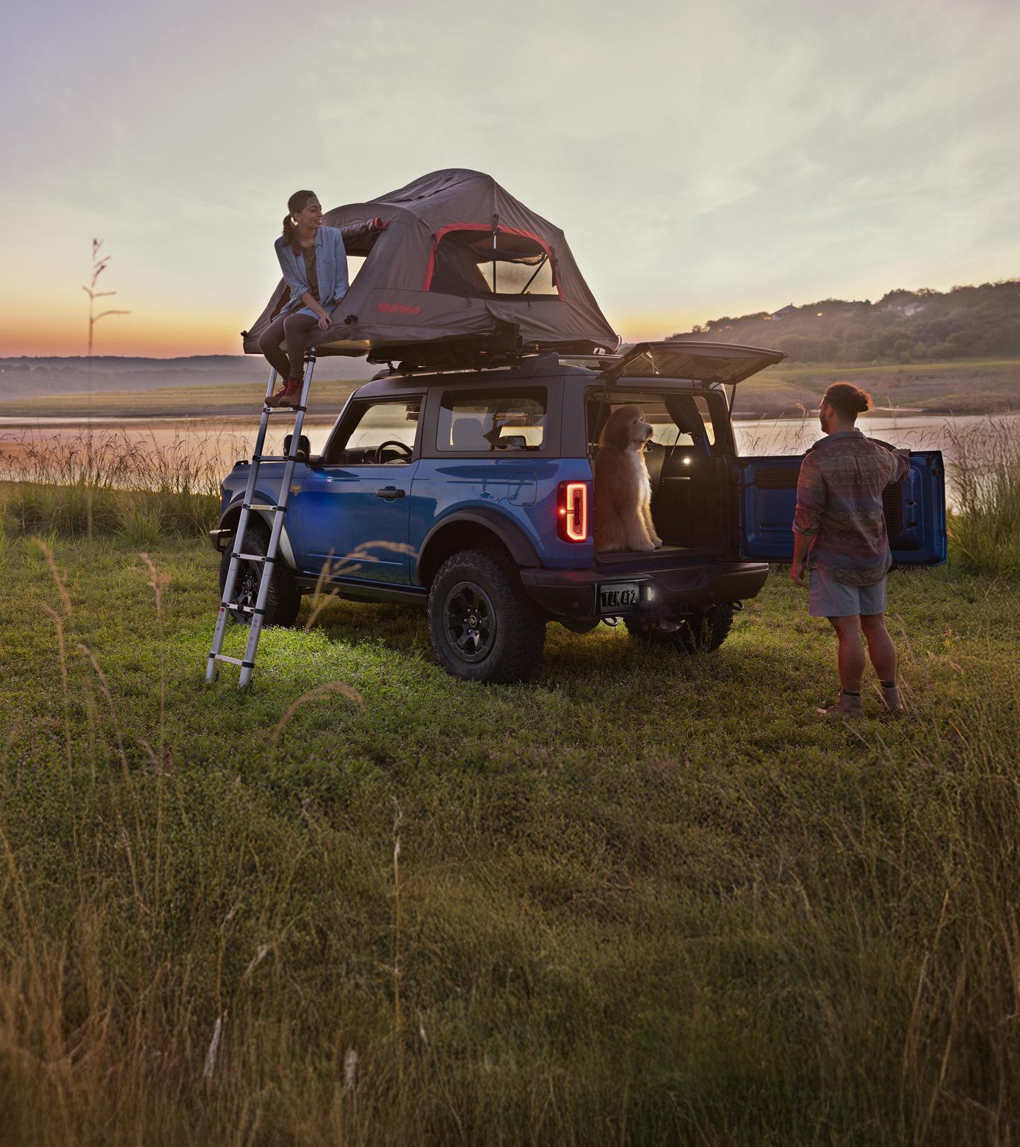 Deux personnes et un chien autour d'un Bronco avec une tente sur le toit.