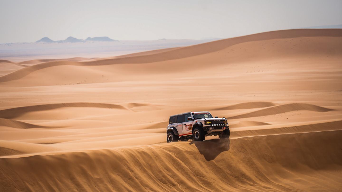 Un Ford Bronco roule sur les dunes d'un désert.