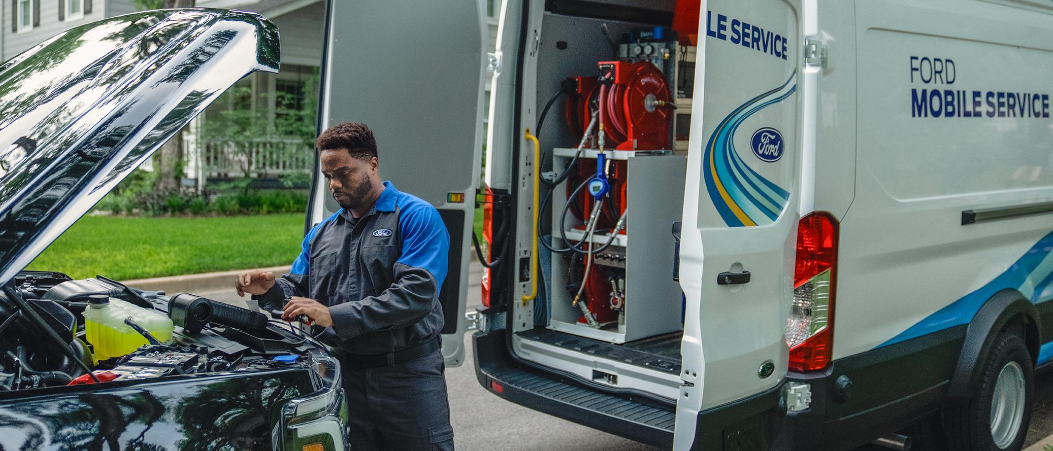 Un technicien du service d’entretien mobile Ford travaille sous le capot d’un camion Ford avec les portes ouvertes d’un fourgon du service mobile derrière lui.