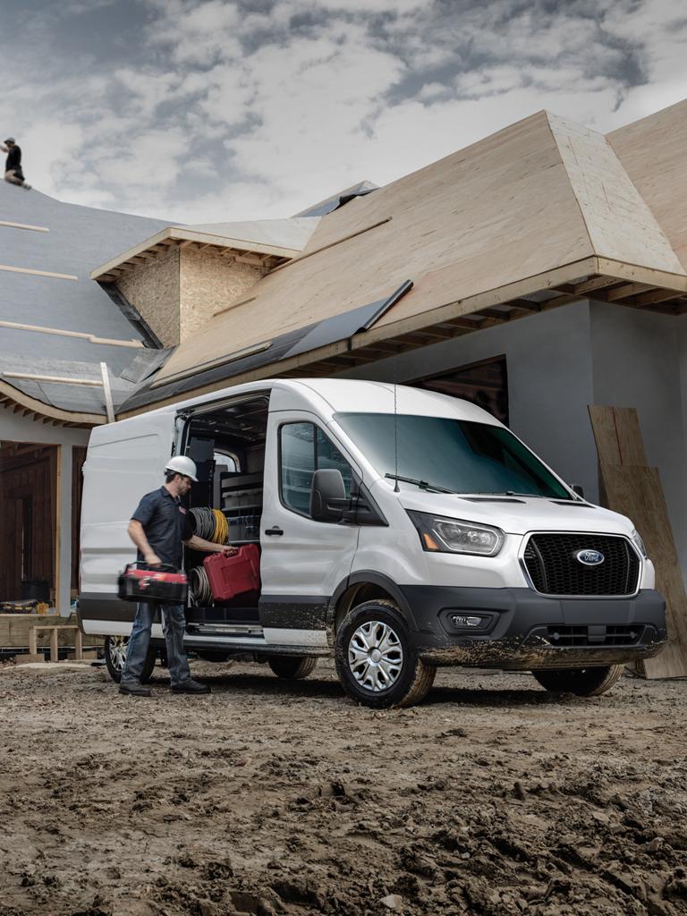 Une fourgonnette de travail Ford Transit® 2027 blanche stationnée sur un chantier de construction résidentielle avec des ouvriers