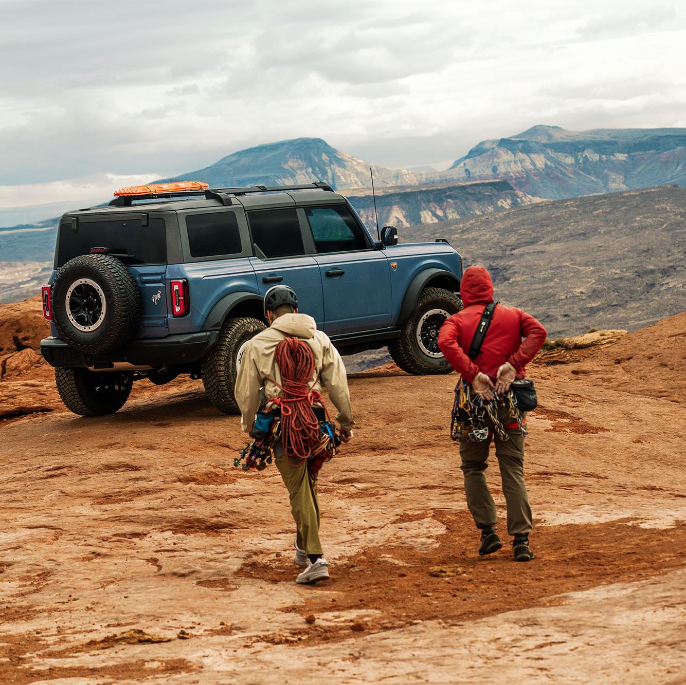 Deux alpinistes masculins marchent vers un Ford Bronco garé sur un terrain rocheux.