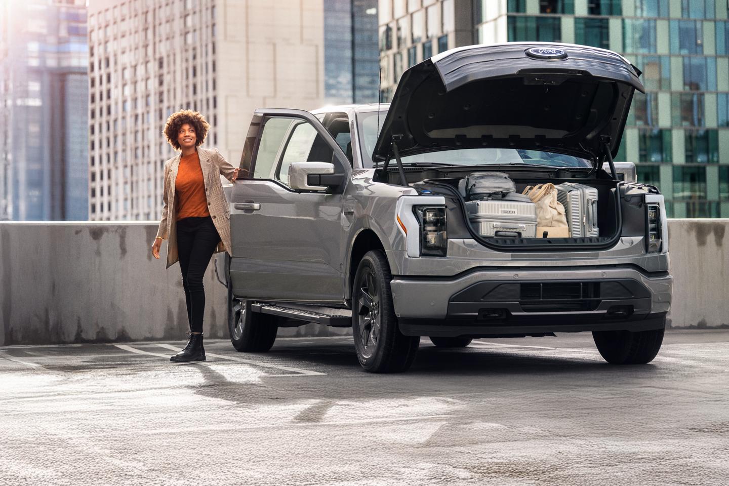 Une femme se tient à côté d'un F-150 Lightning dont le coffre est ouvert et rempli de bagages.