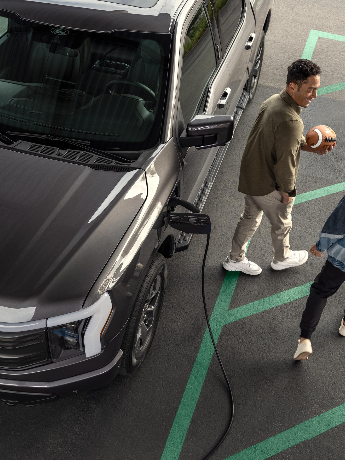 Un couple s’éloigne de son Ford F-150 Lightning en cours de recharge dans un stationnement avec une icône de chargement superposée.