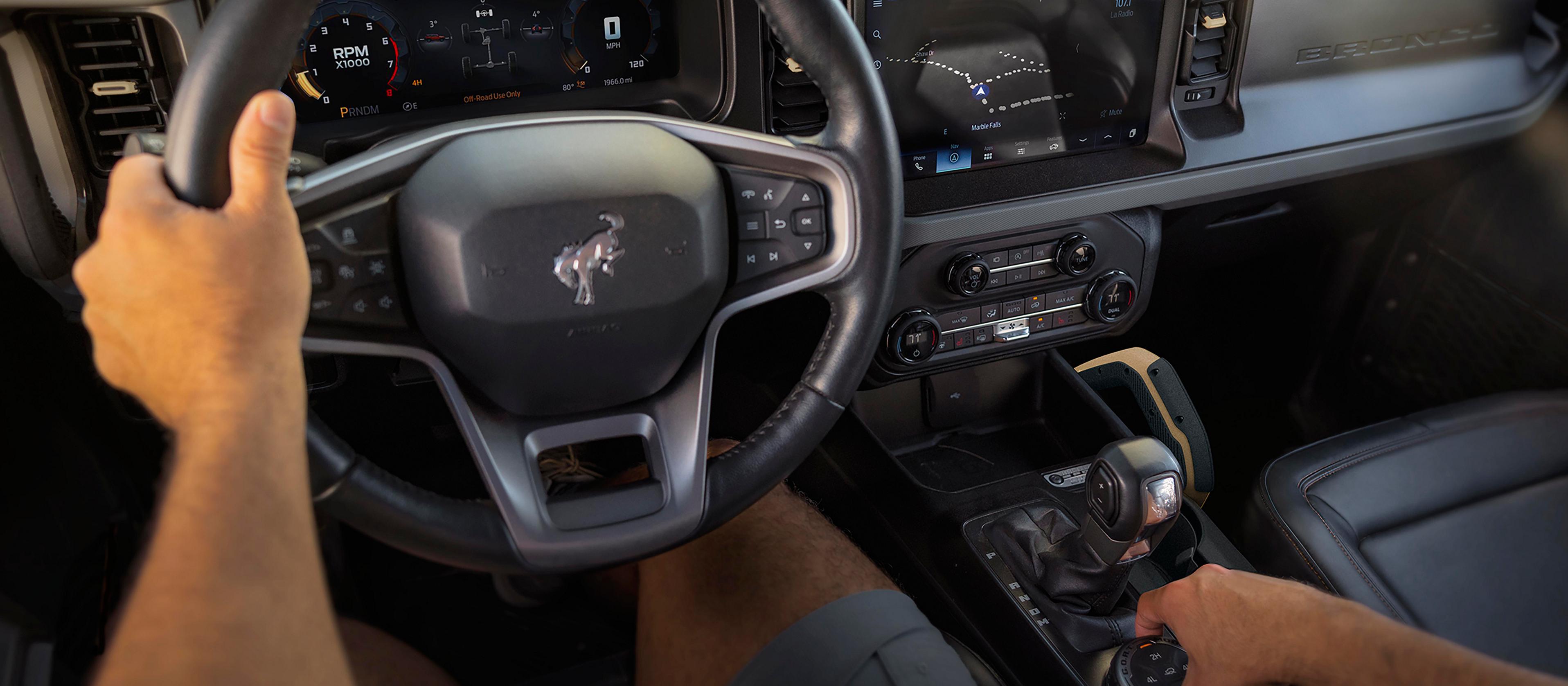 Le tableau de bord d’un VUS Ford Bronco® 2026, avec les mains du conducteur visibles sur le volant et le sélecteur de mode de conduite