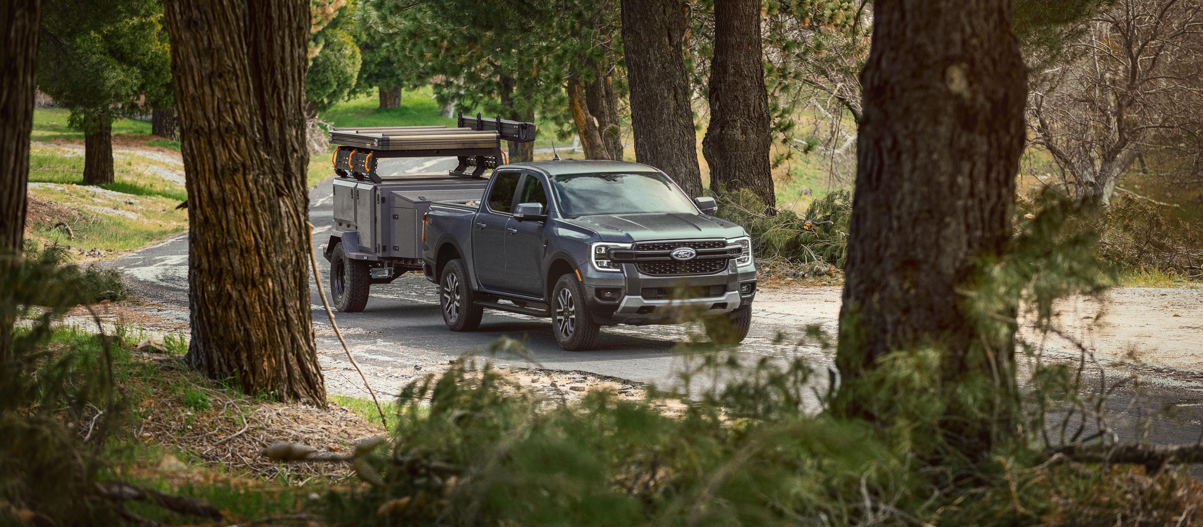 Un modèle Ford Ranger® 2025 gris tirant une remorque le long d’une route boisée