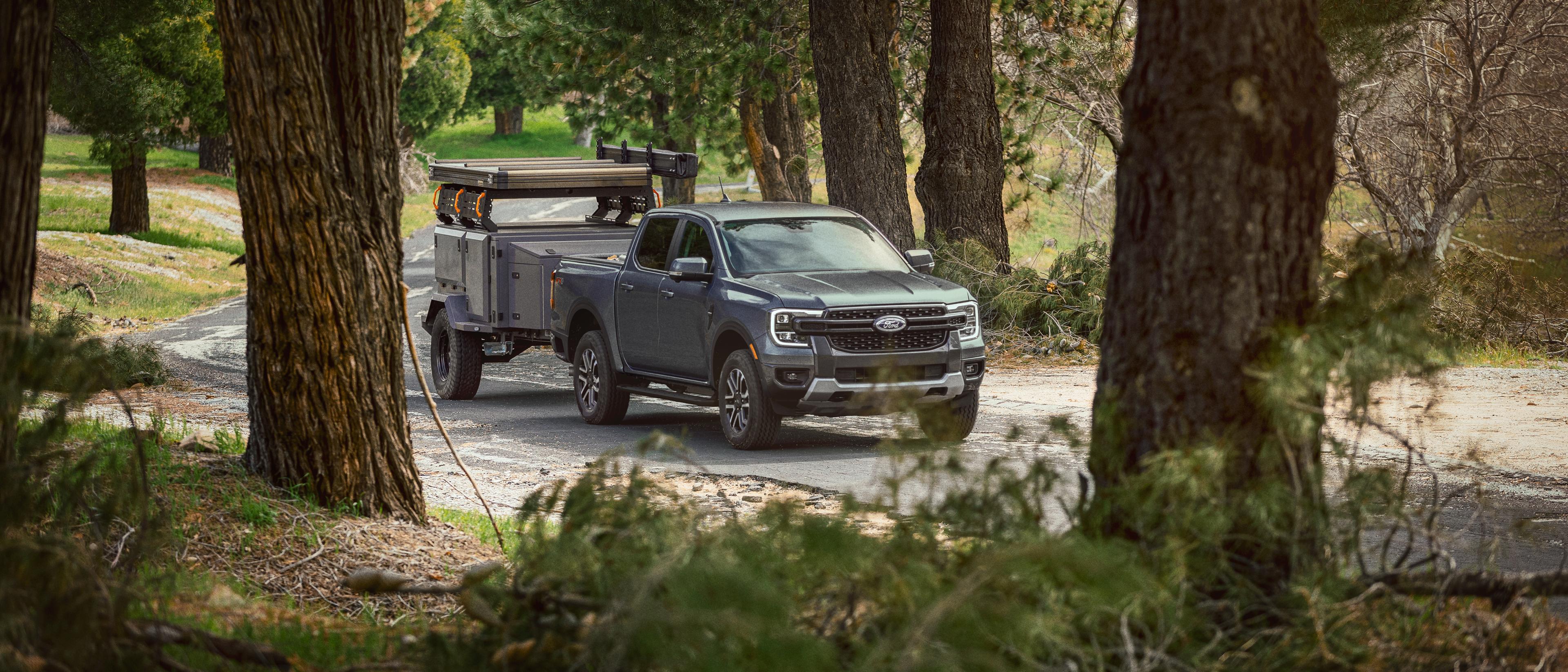 Un modèle Ford Ranger® 2025 gris carbonisé tirant une remorque le long d’une route boisée