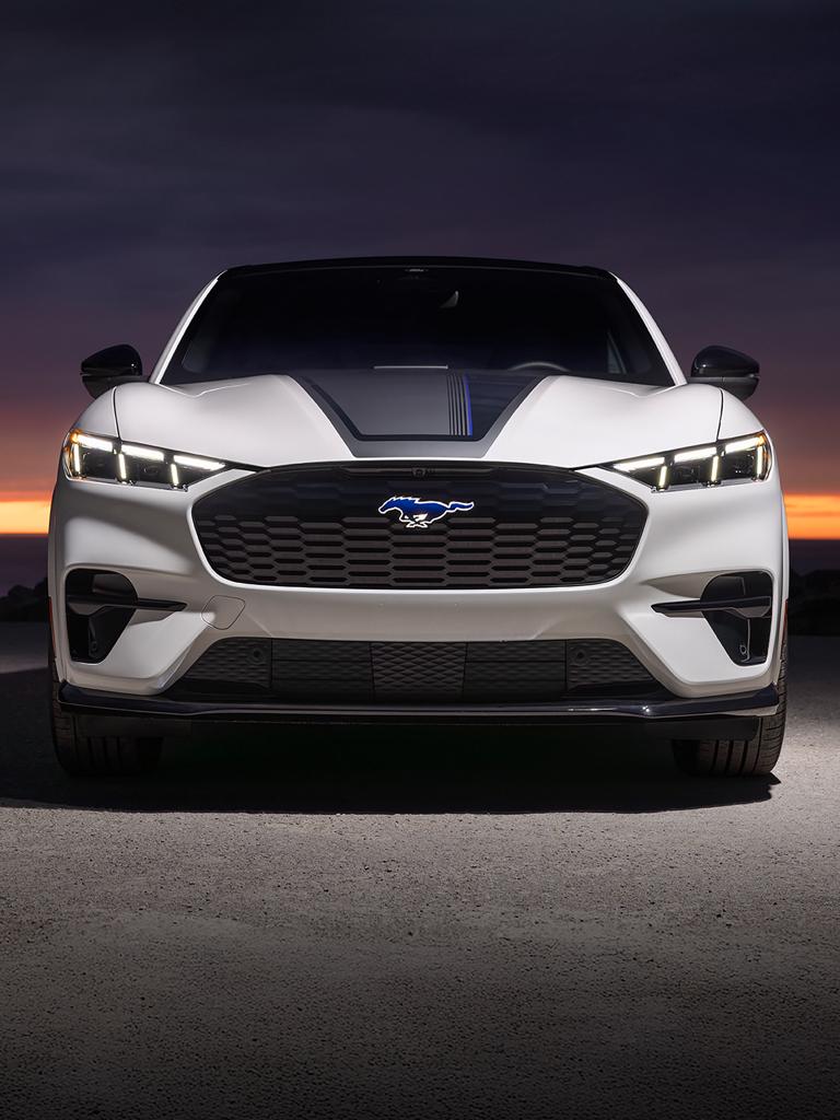 Extrémité avant d’un modèle Ford Mustang Mach-E® GT 2026 avec bande sur le capot sur fond de coucher de soleil