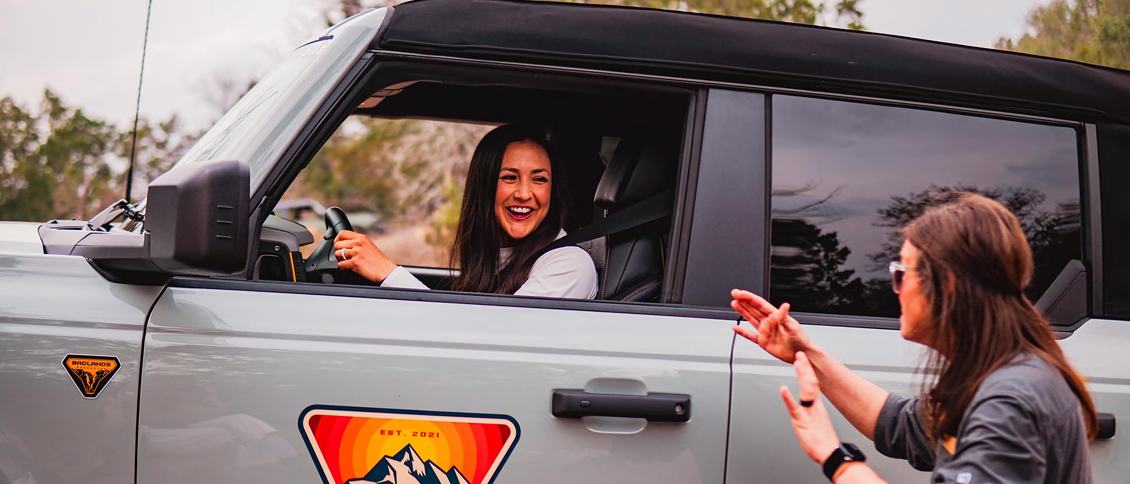 Une femme conduisant un VUS Ford Bronco® 2025 lors d’une expérience Bronco Off-Roadeo®, avec un instructeur donnant des directives de l’extérieur du véhicule