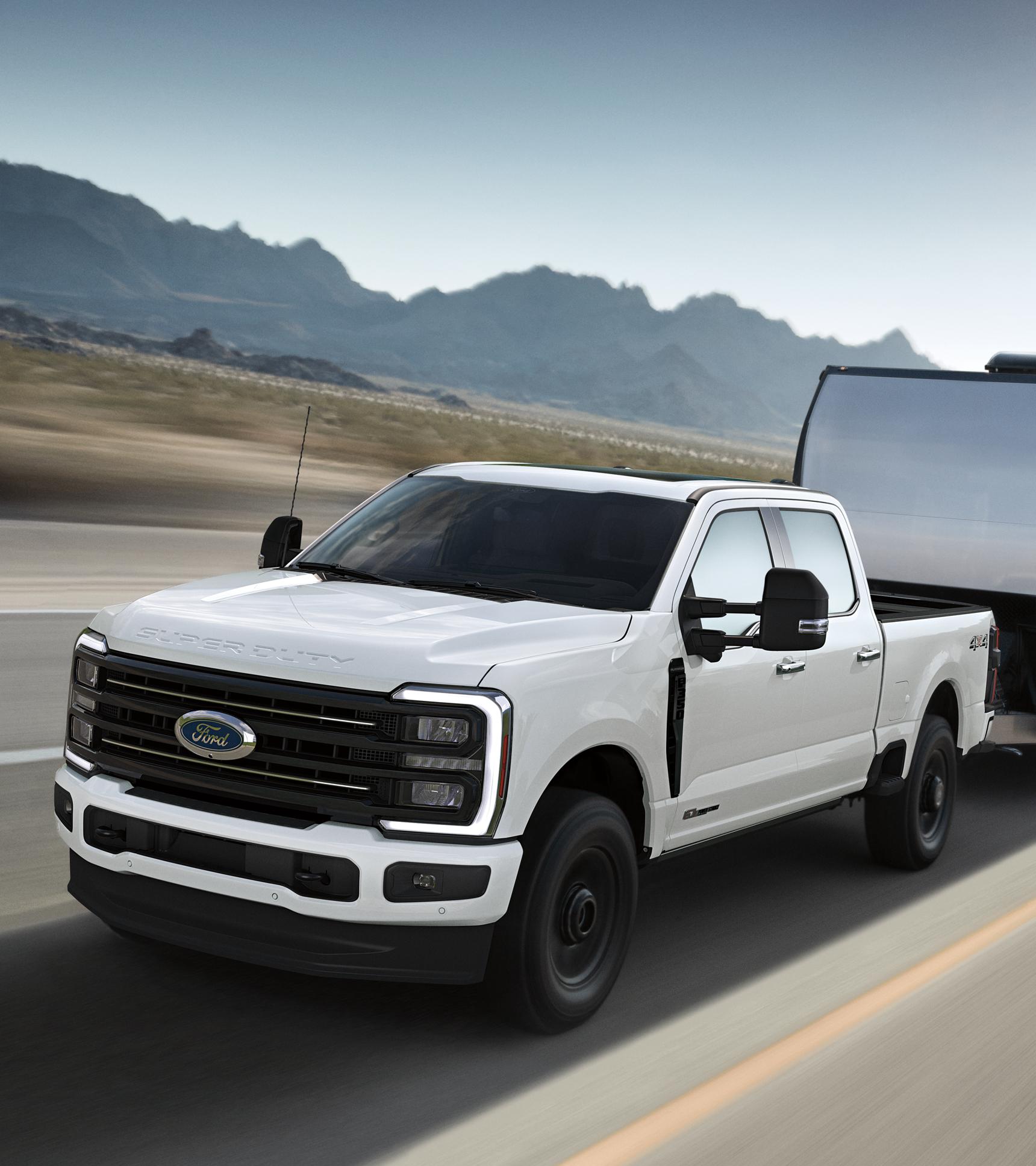 Modèle Ford Super Duty® F-350® Platinum® 2026 en blanc étoilé circulant sur une route pavée tout en tirant une grande remorque argentée