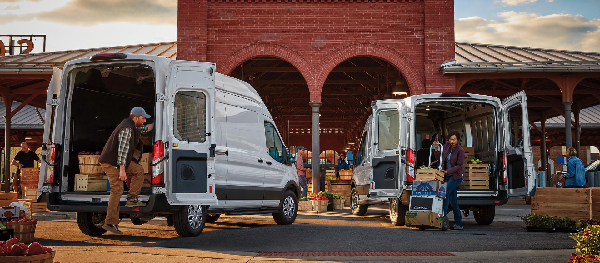 Deux fourgonnettes Ford Transit® blanches, portes arrière ouvertes, avec des personnes déchargeant des produits dans un marché