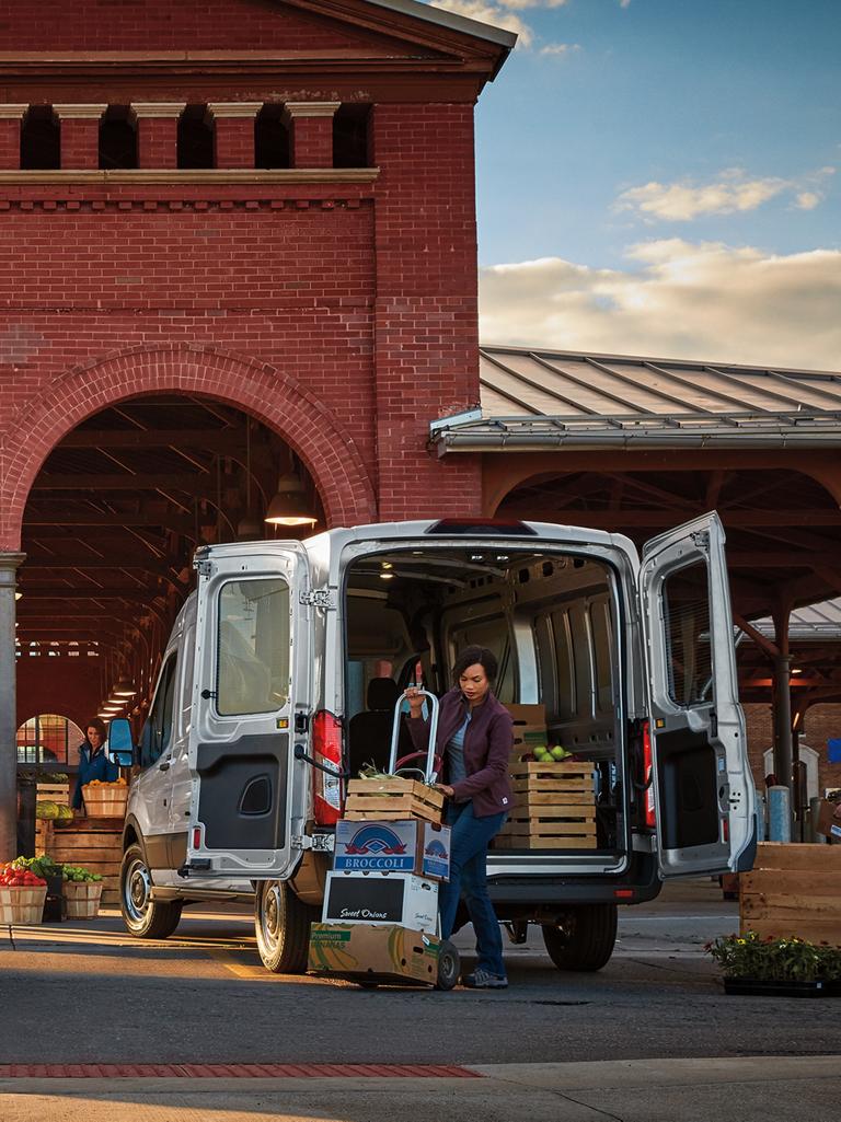 Deux fourgonnettes utilitaires Ford Transit® 2027 blanches chargées de produits frais dans un marché en plein air