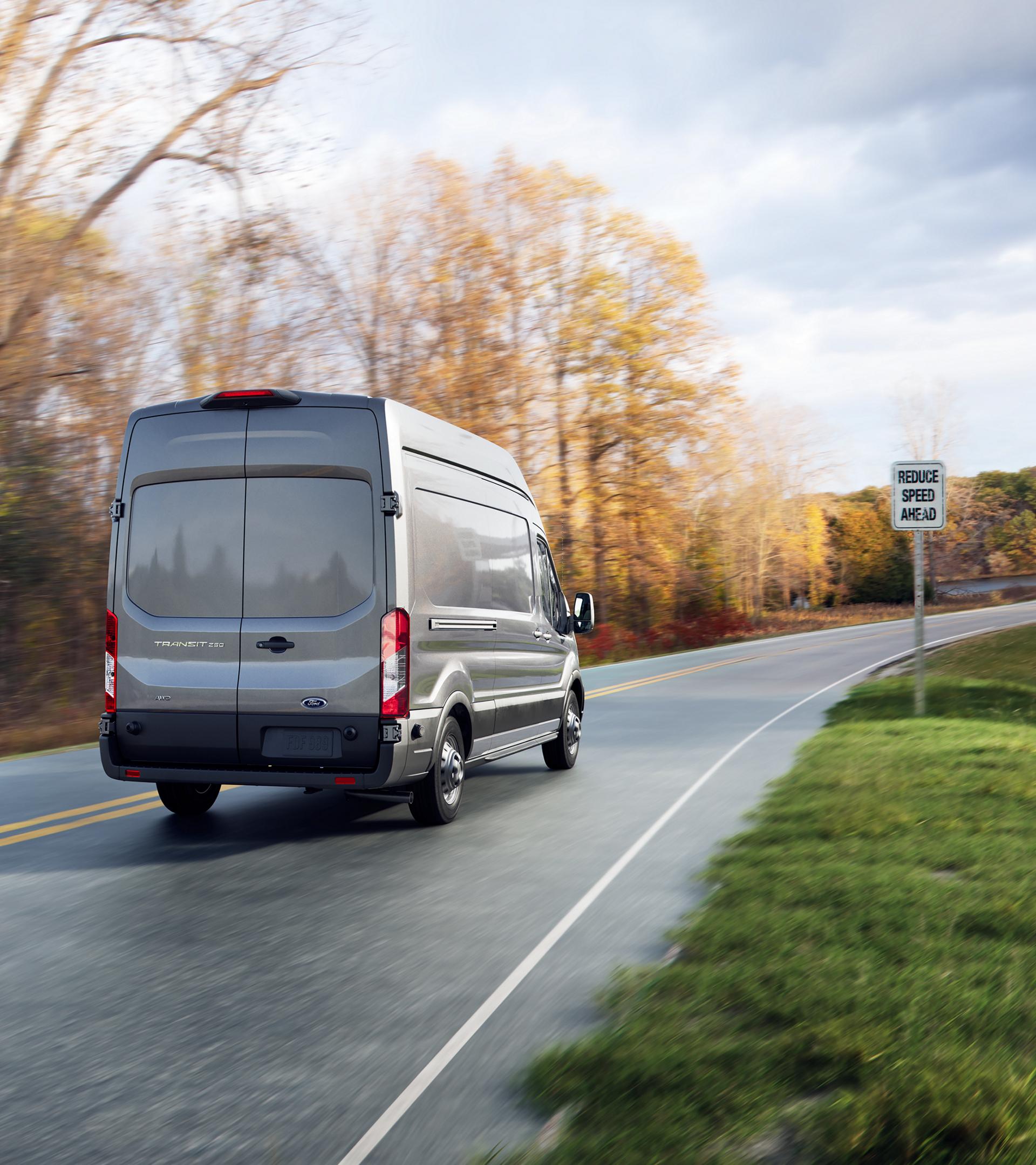 Vue arrière d’une fourgonnette Ford Transit® 2025 conduite sur une route avec un panneau de limite de vitesse