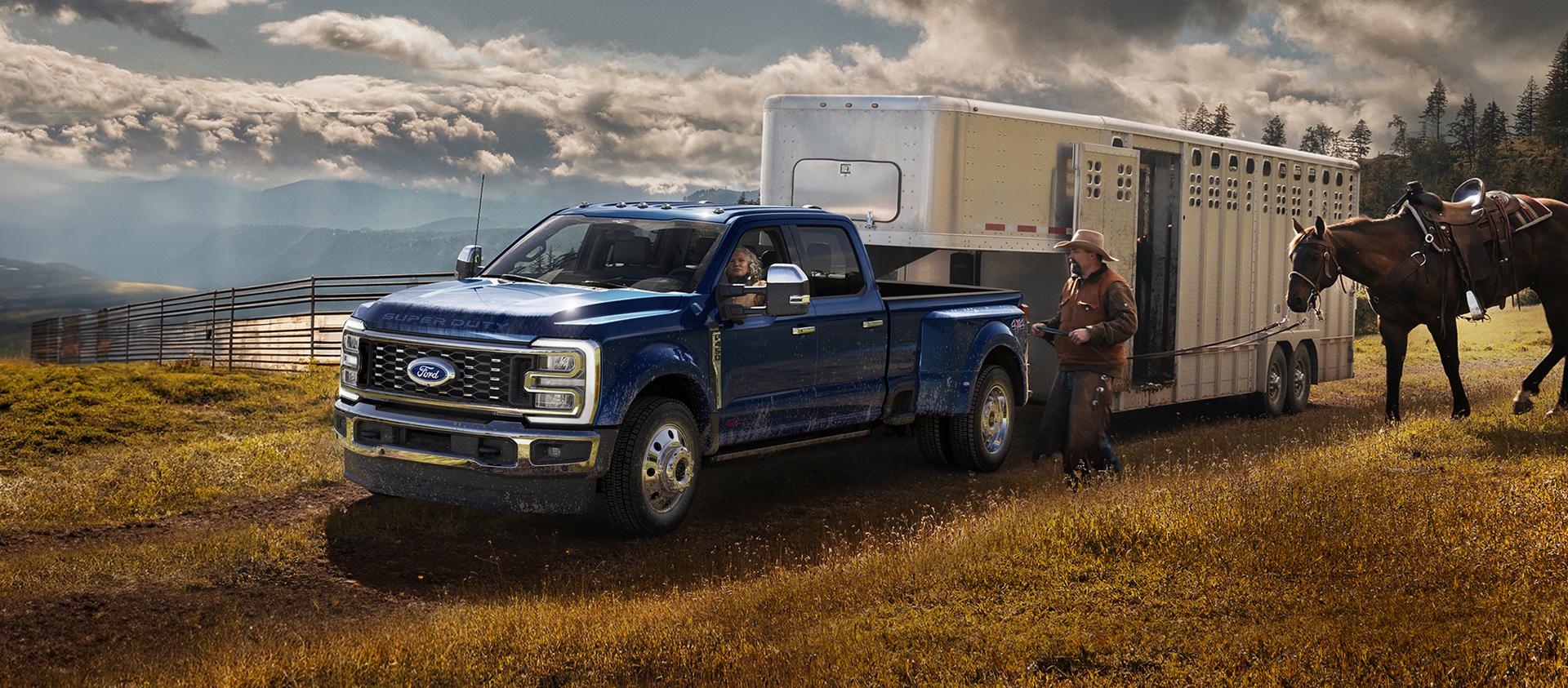 Modèle Ford Super Duty® F-450® King Ranch® 2026 en bleu argon remorquant un transporteur de chevaux sur une ferme herbeuse