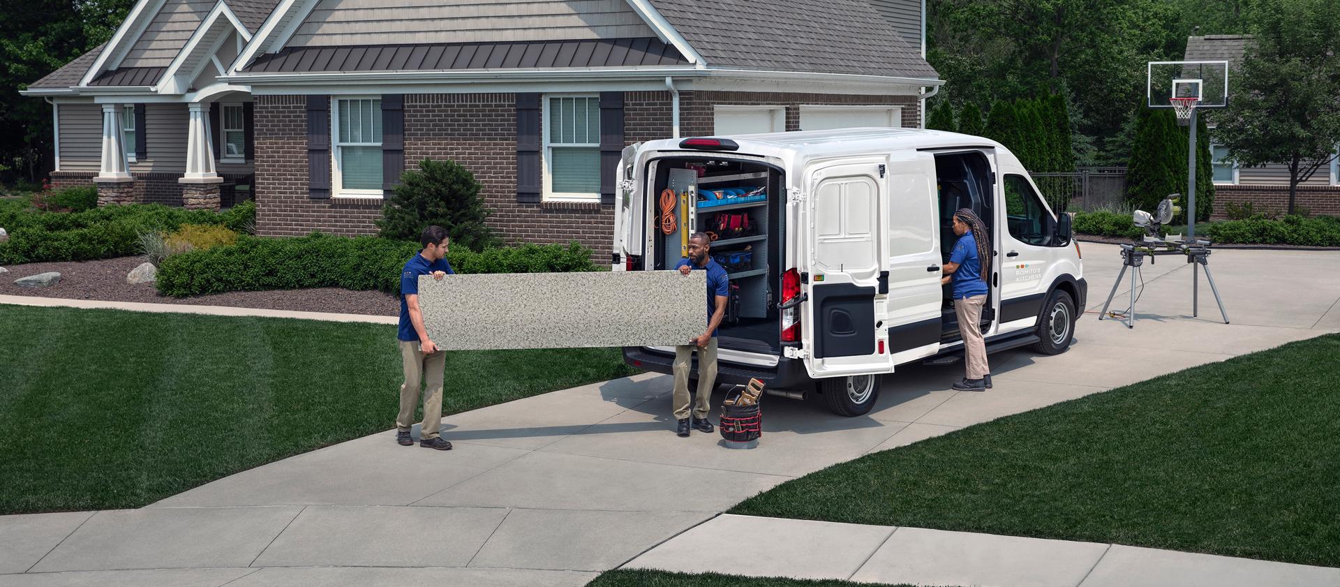 Des techniciens de service déchargent de l’équipement d’une fourgonnette utilitaire Ford Transit® 2027 blanche dans une entrée de garage