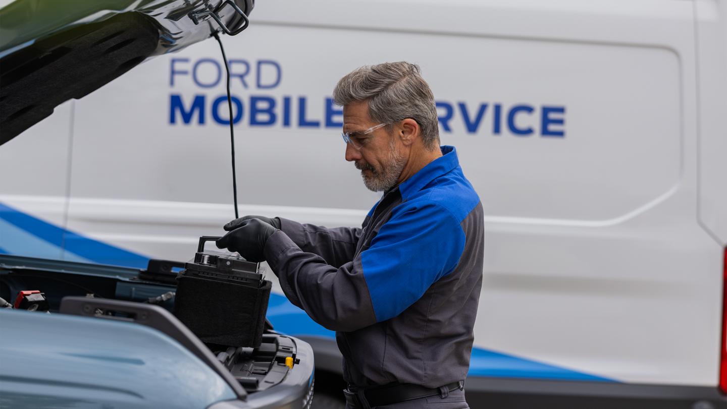 Un technicien de Service Ford intervient sur le moteur d’un véhicule. Le fourgon du service d’entretien mobile est visible en arrière-plan.