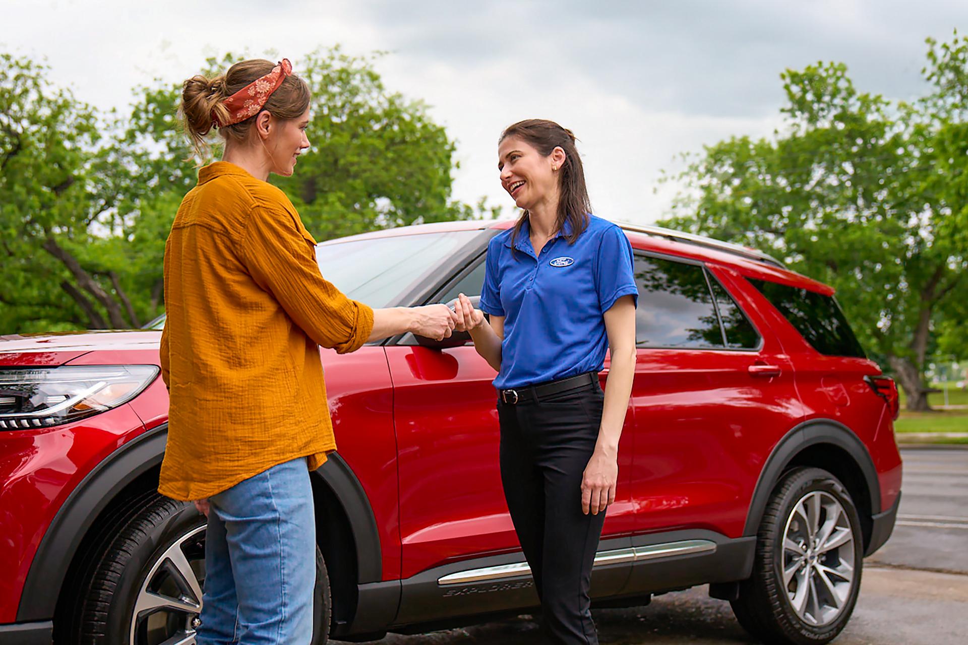 Une employée de Service Ford tend des clés à une cliente à côté d’un véhicule Ford.