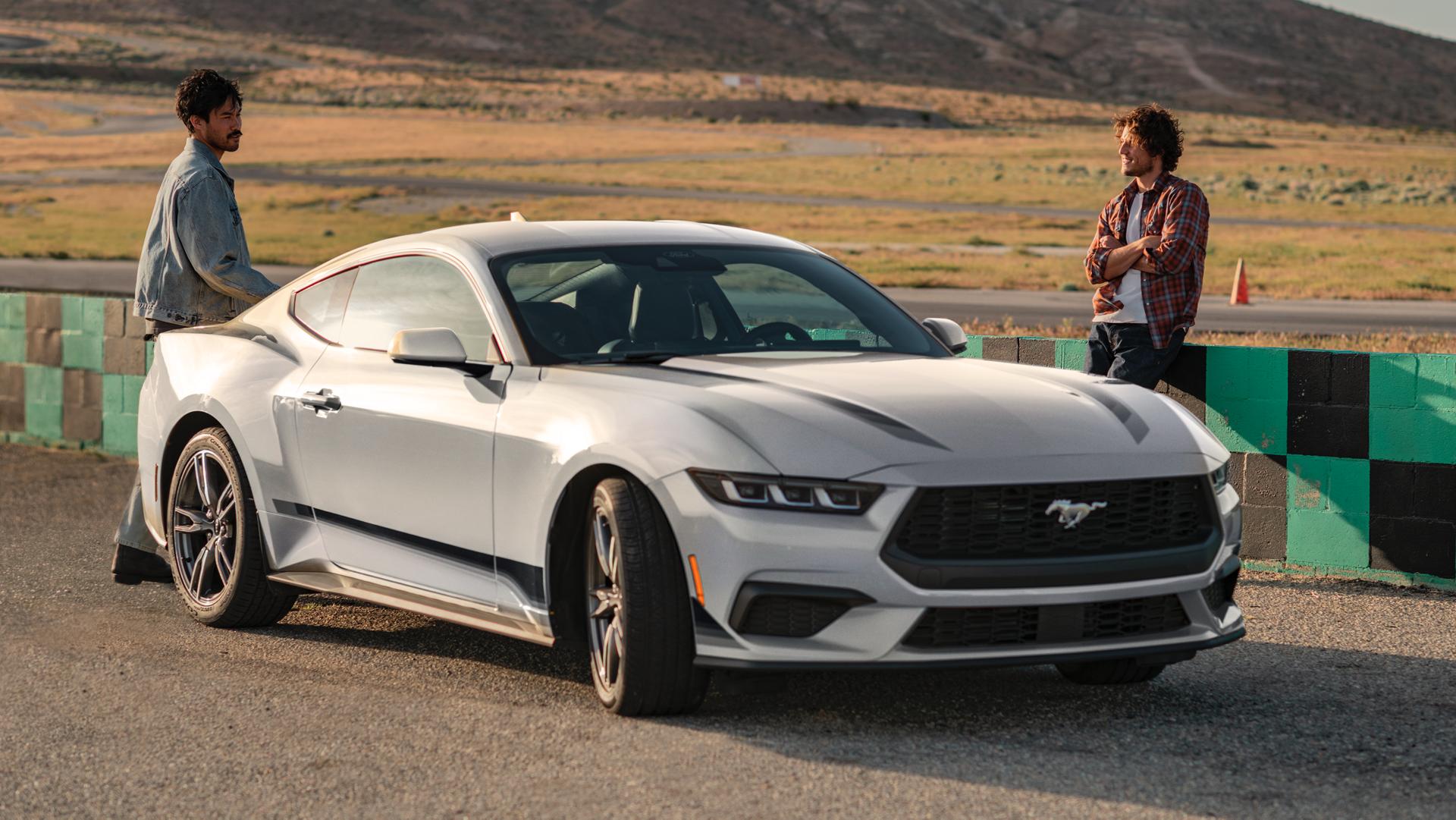 Ford Mustang® EcoBoost® Coupé 2025 avec ensemble jantes et bandes en option stationnée sur un terrain de course près de personnes
