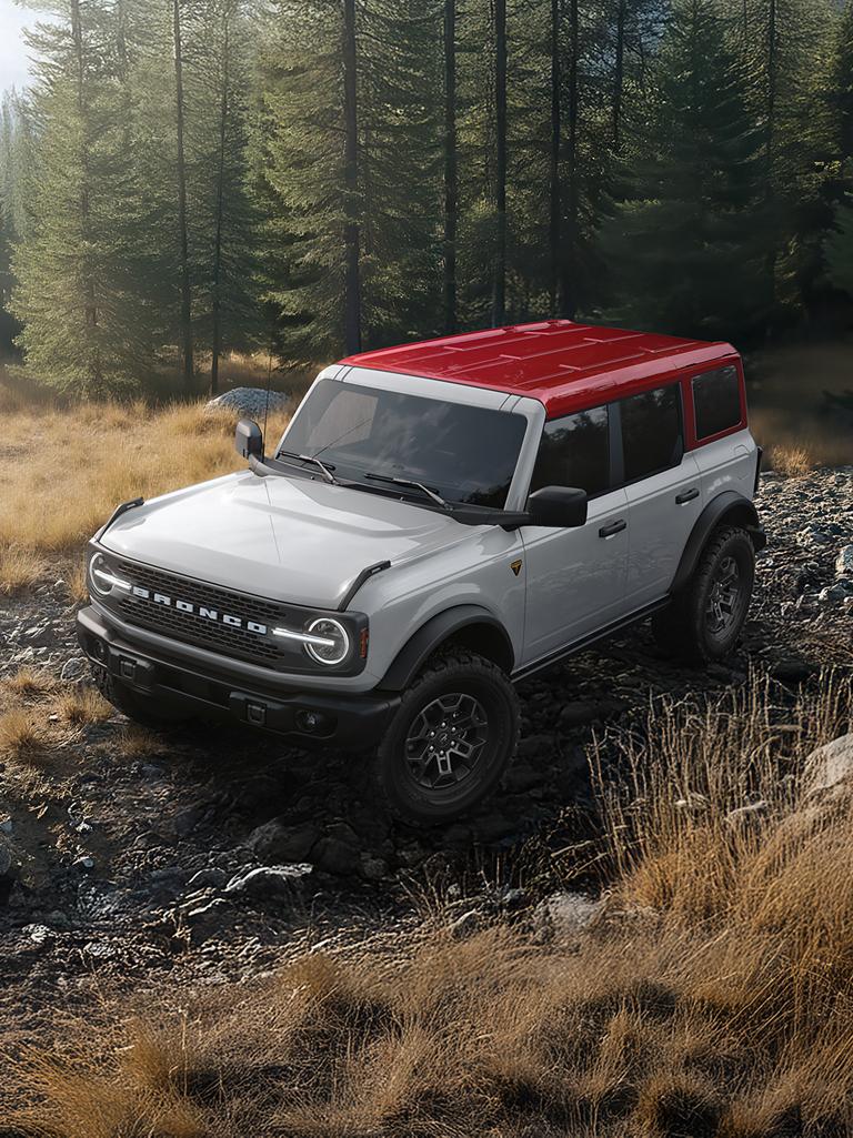 Un VUS Ford Bronco® sur un chemin boueux, avec une carrosserie de couleur sombre et un toit rouge.