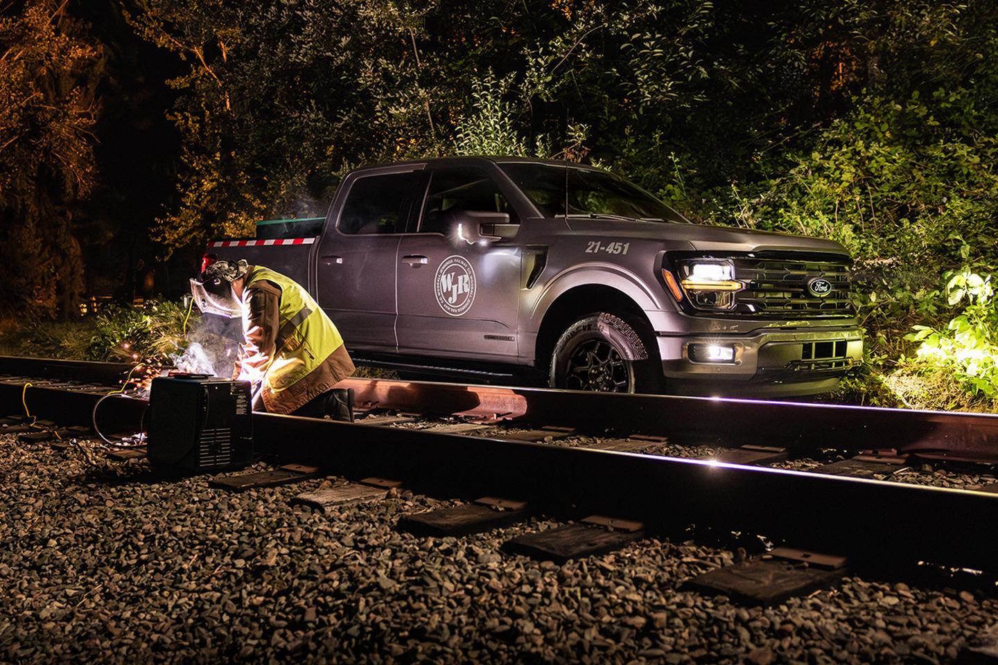 Une personne soude une voie ferrée de nuit, près d'un F-150 garé.