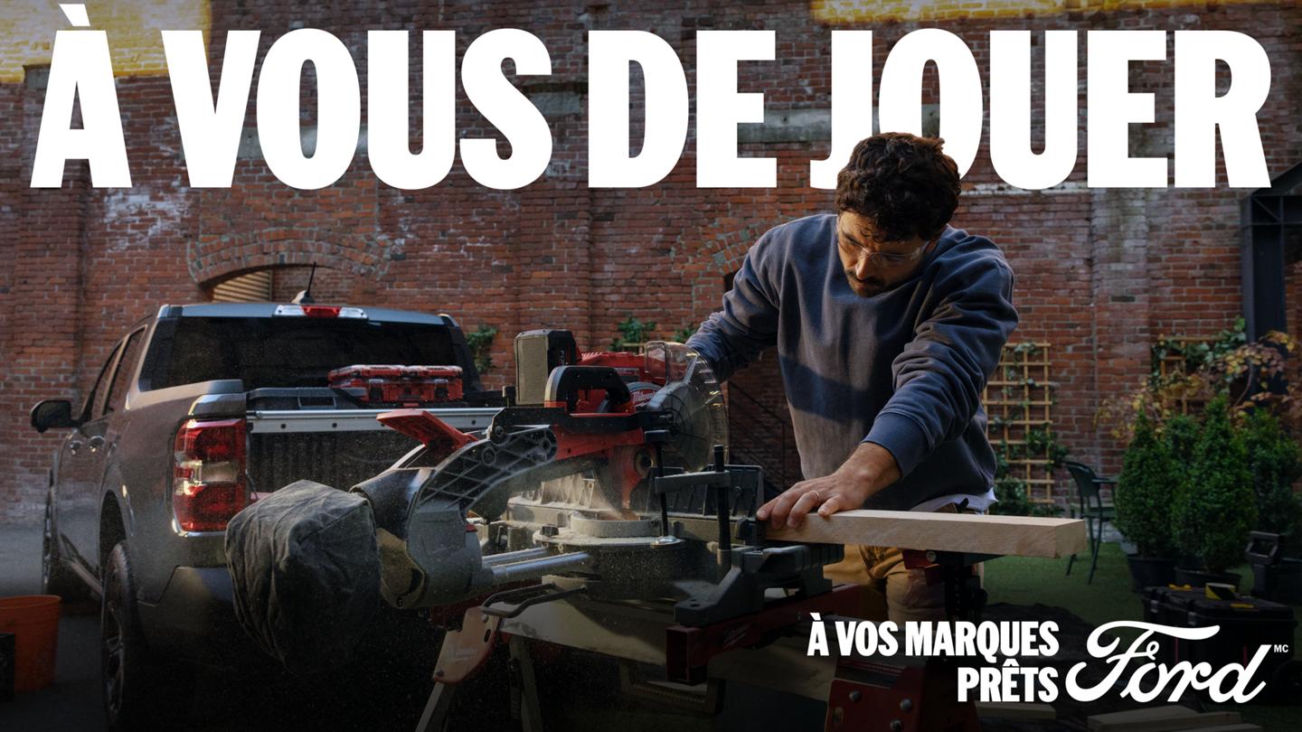 Un homme coupe du bois avec une scie à onglets électrique devant un camion Ford Maverick 2026 de couleur gris carbonisé près d’un édifice en briques. On peut lire le titre « À VOUS DE JOUER ».