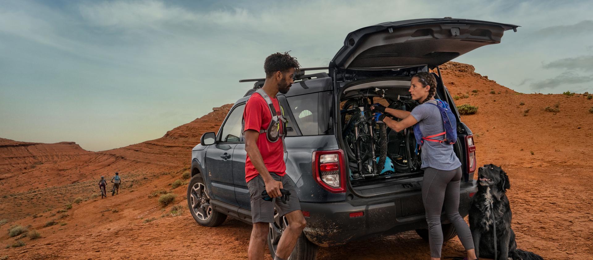 VUS Ford Bronco Sport® 2026 garé dans le désert, avec deux personnes en tenue de randonnée et leur chien à l’extérieur.