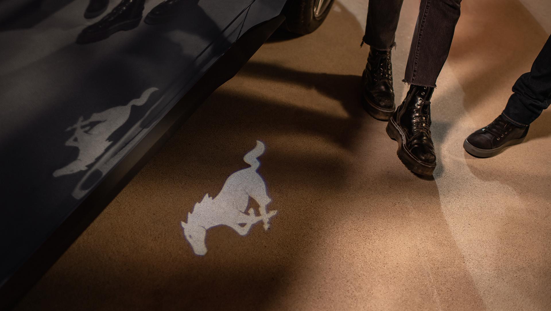 Deux personnes debout près d’un modèle Ford Mustang® 2026 avec projecteurs de logo de poney en option