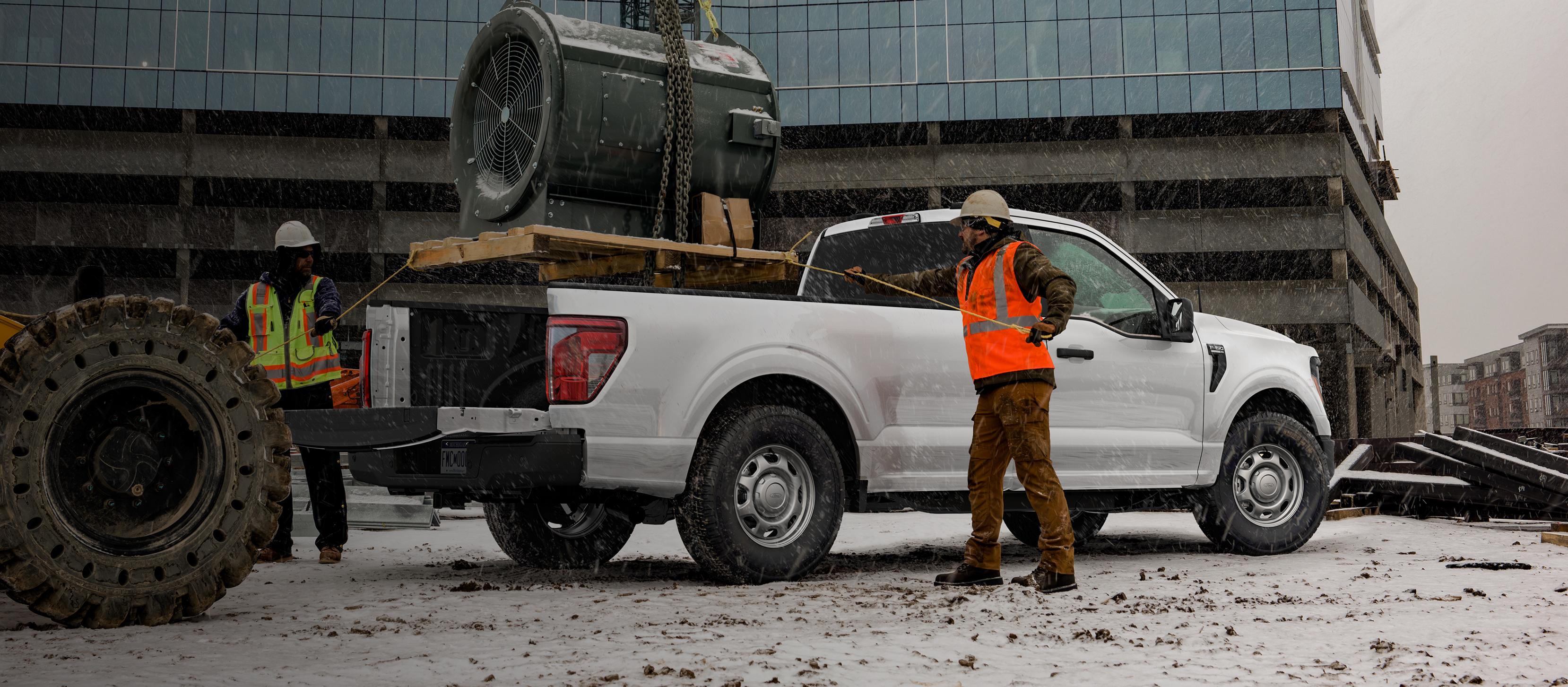 Deux travailleurs de la construction attachent une cargaison dans la caisse d’une camionnette Ford F-150® 2025 stationnée sur un chantier