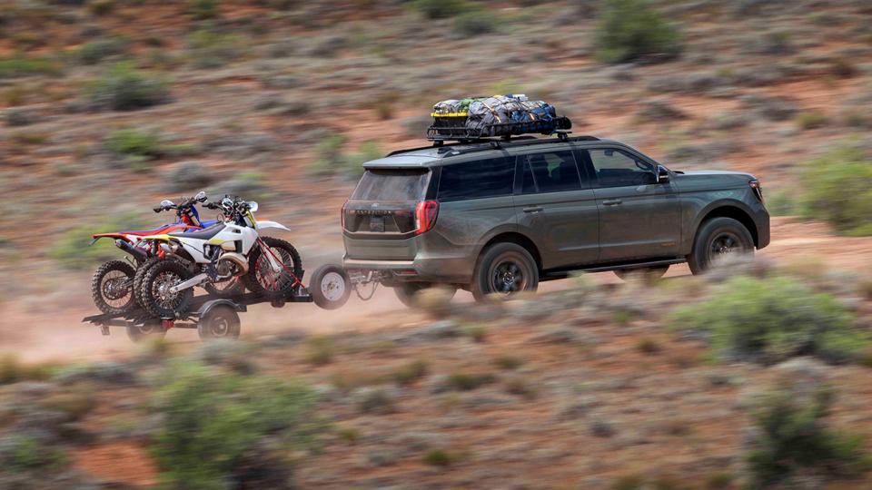 Modèle Ford Expedition® Tremor® 2025 avec un conducteur tirant une remorque de moto tout-terrain sur une route désertique