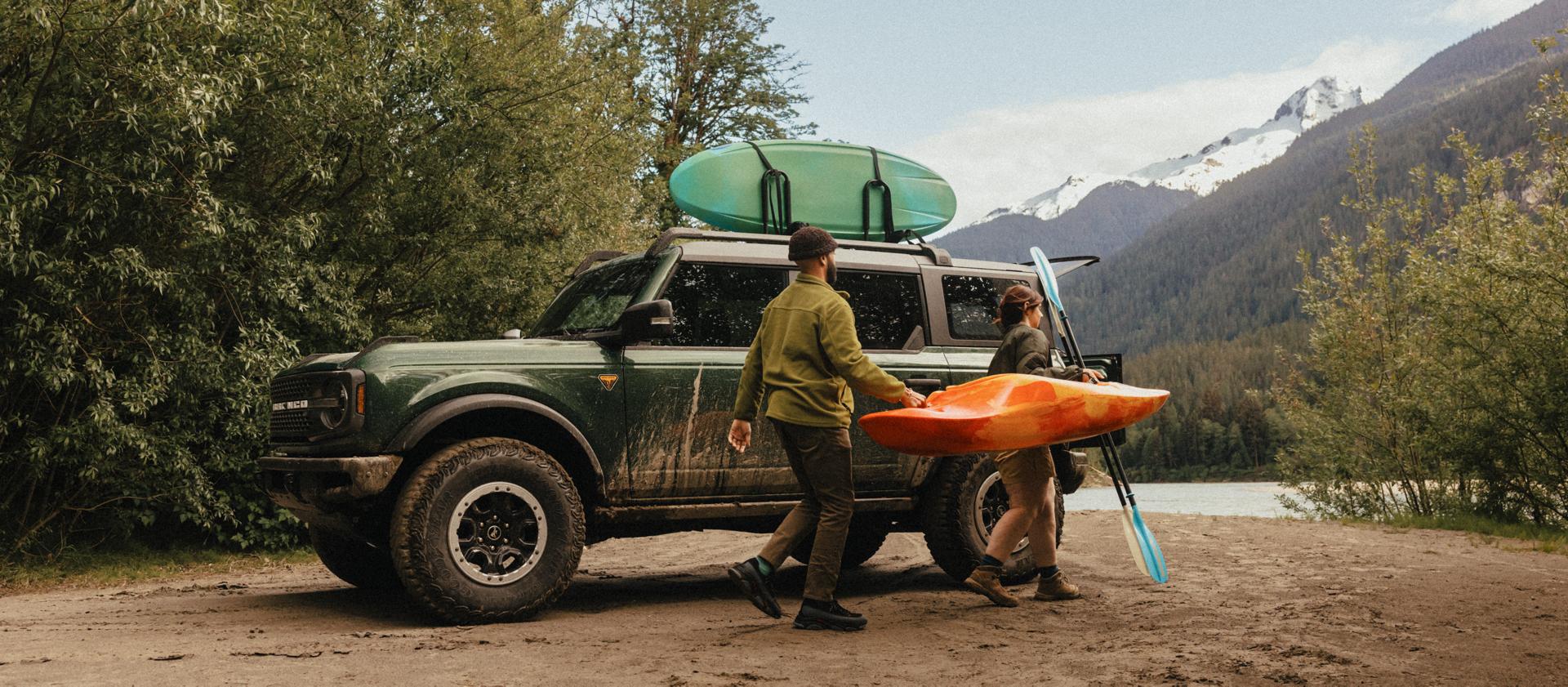 Deux personnes transportant un kayak près d’un VUS Ford Bronco® 2025 stationné près d’un ruisseau de montagne