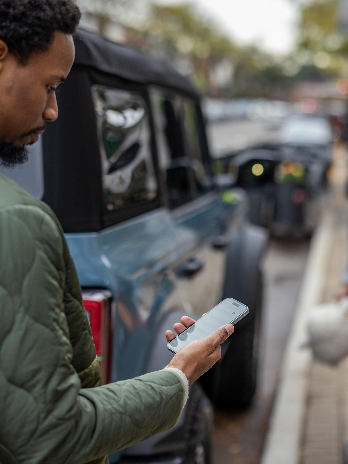 Une personne se tenant près d’un Ford Bronco utilise un téléphone intelligent.