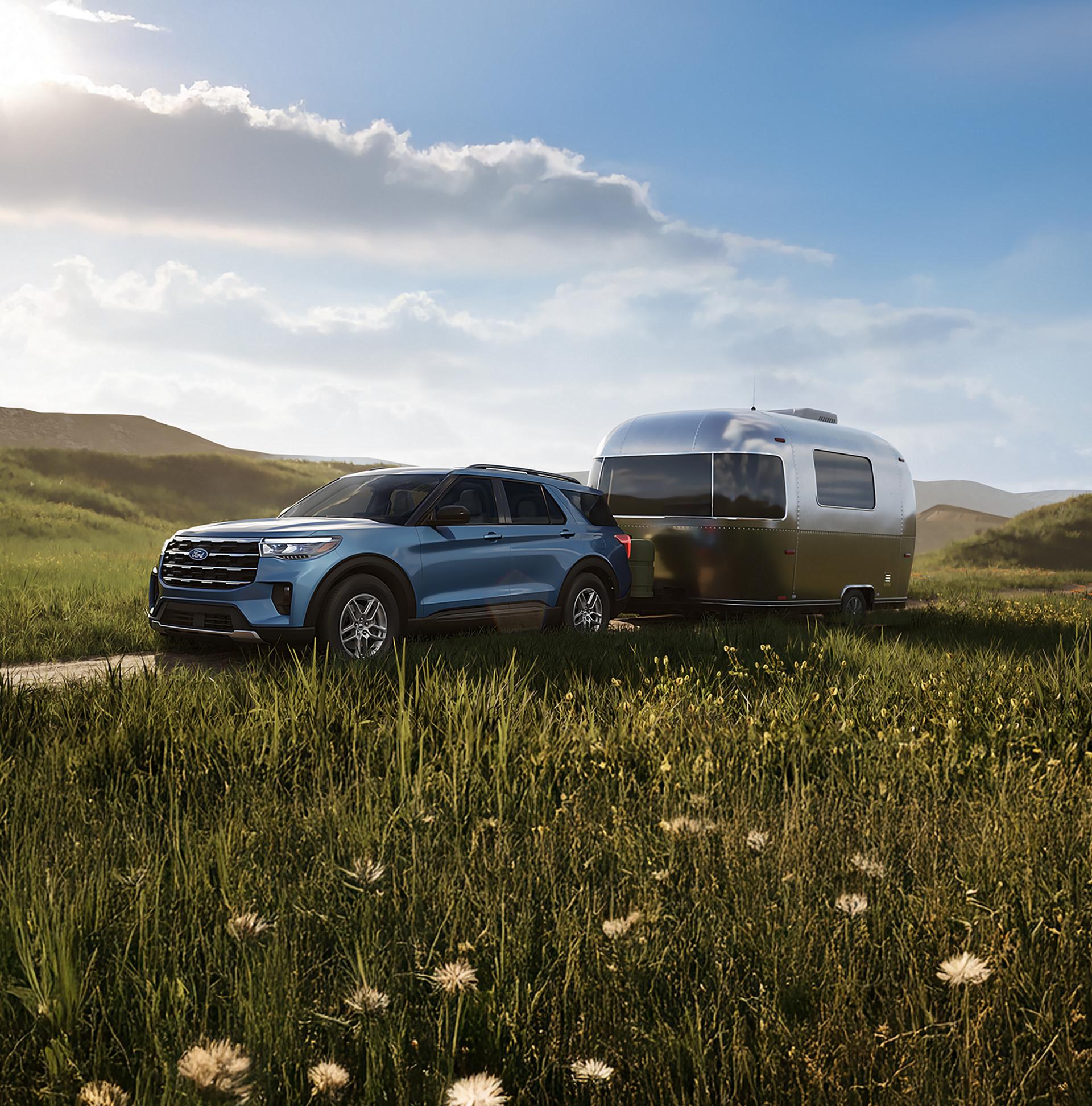 Un VUS Ford Explorer® 2027 tirant une caravane sur une route traversant une prairie