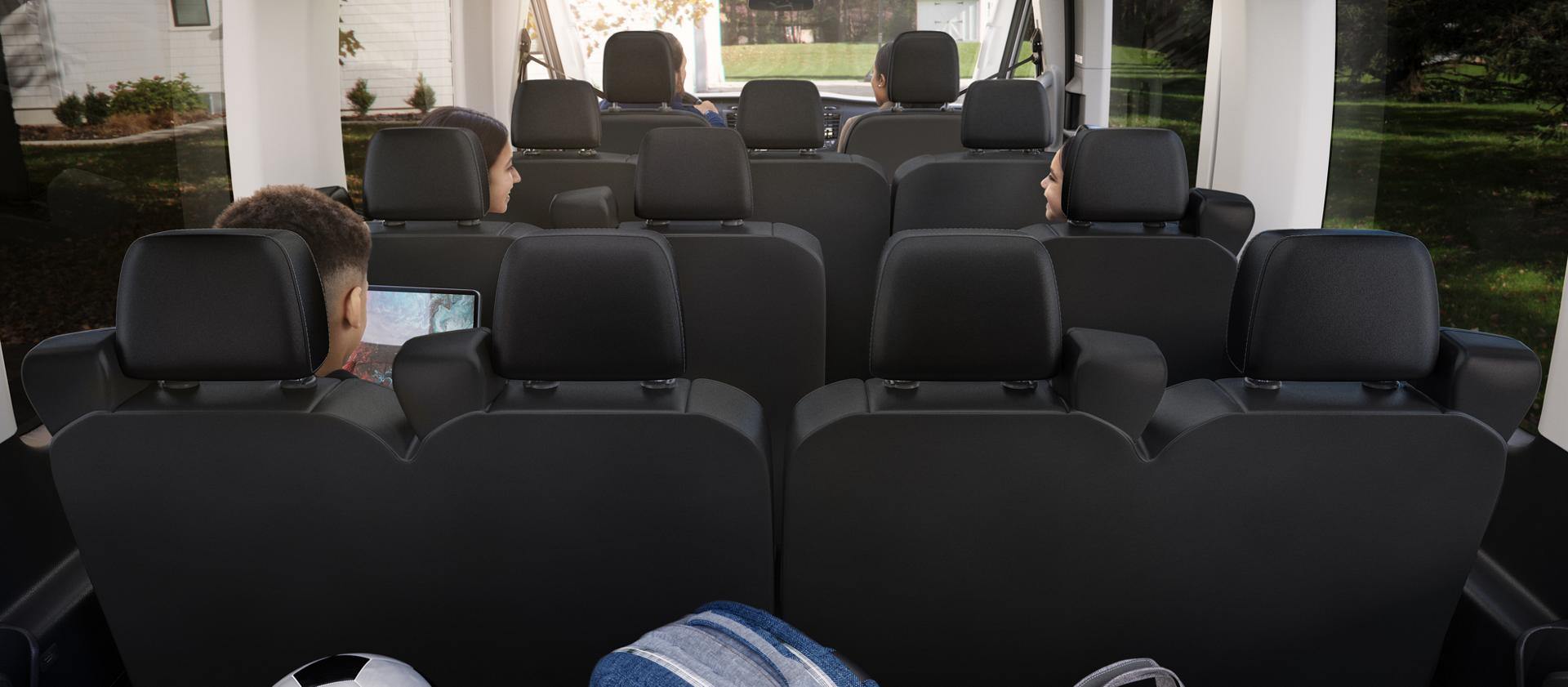 Vue arrière de l’intérieur d’une fourgonnette de transport de passagers Ford Transit® 2027 montrant plusieurs rangées de sièges occupés par des passagers et du matériel de sport