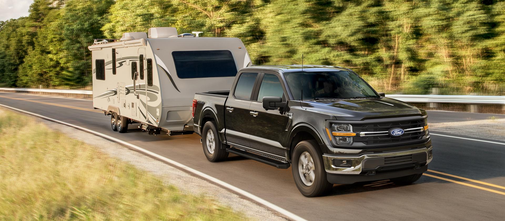 Camion Ford F-150® XLT 2025 tirant une remorque de camping sur une route bordée d’arbres