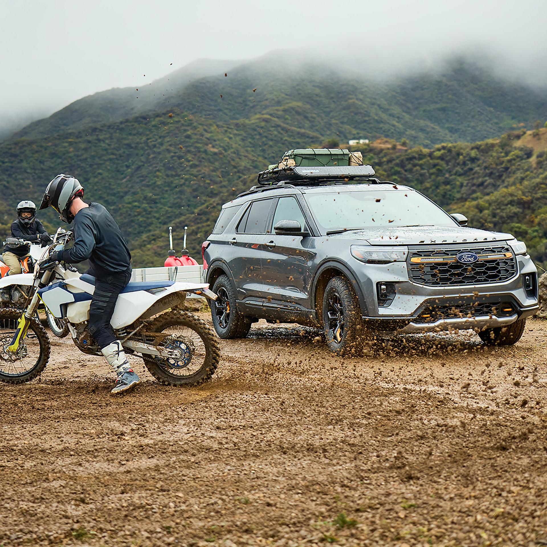 Un pilote soulevant de la boue avec les jantes de sa moto hors route, près d’un VUS Ford Explorer® Tremor® 2027 stationné