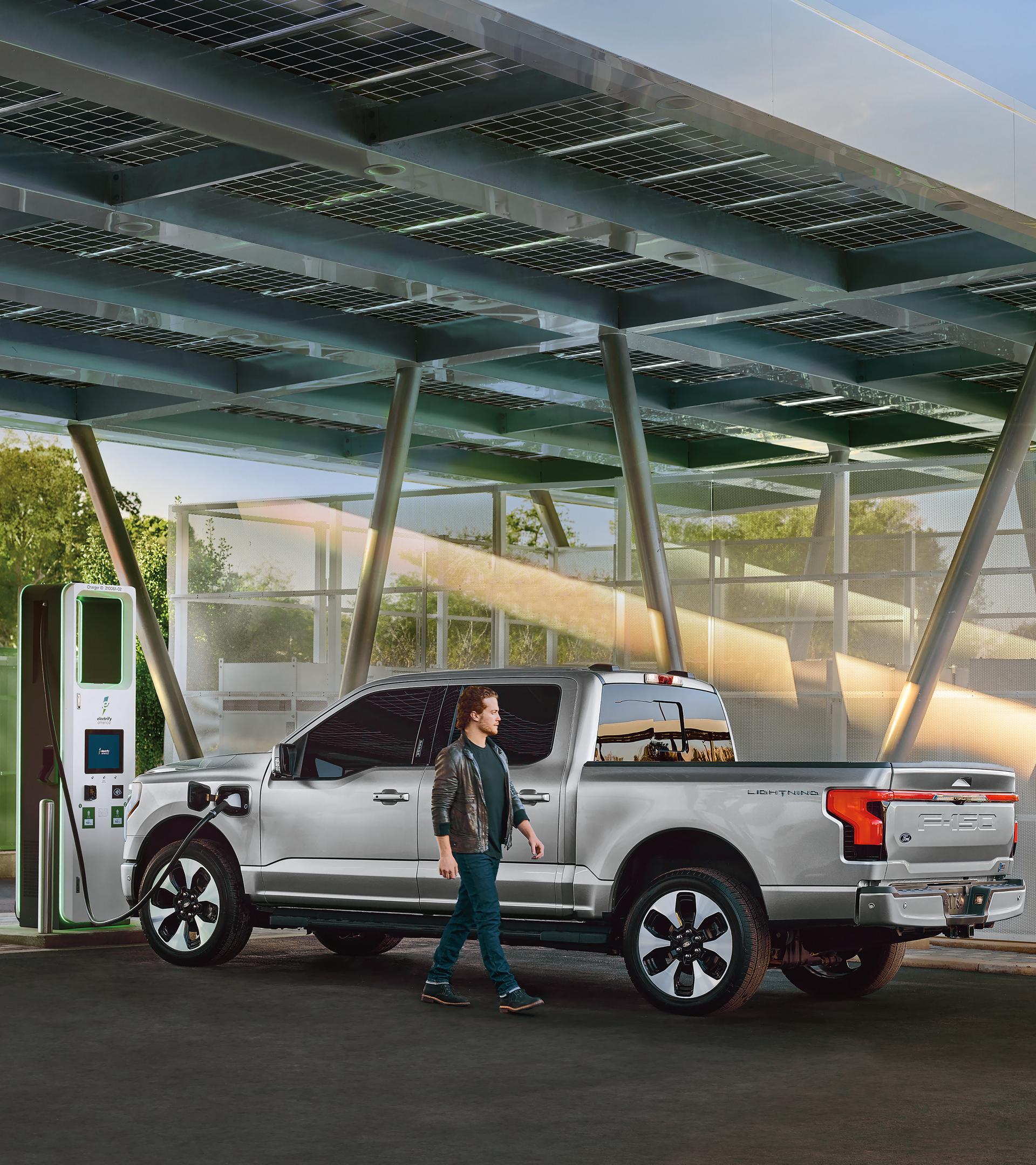 Une personne passe devant un F-150 Lightning branché à une borne de recharge publique.