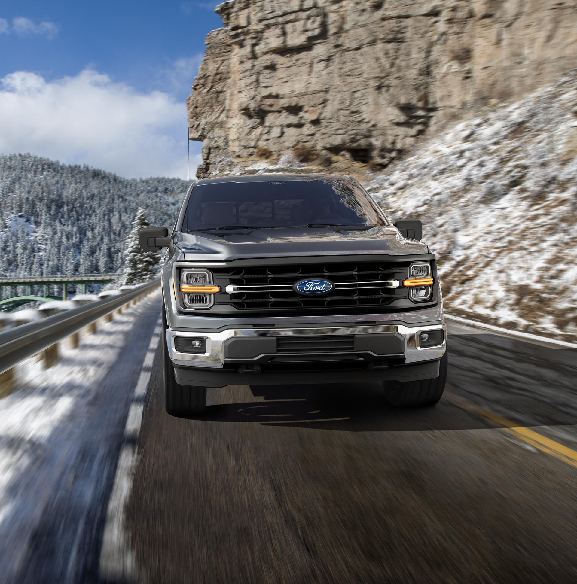 Modèle Ford F-150® Lariat® 2026 conduit sur une route de montagne avec des montagnes couvertes de neige